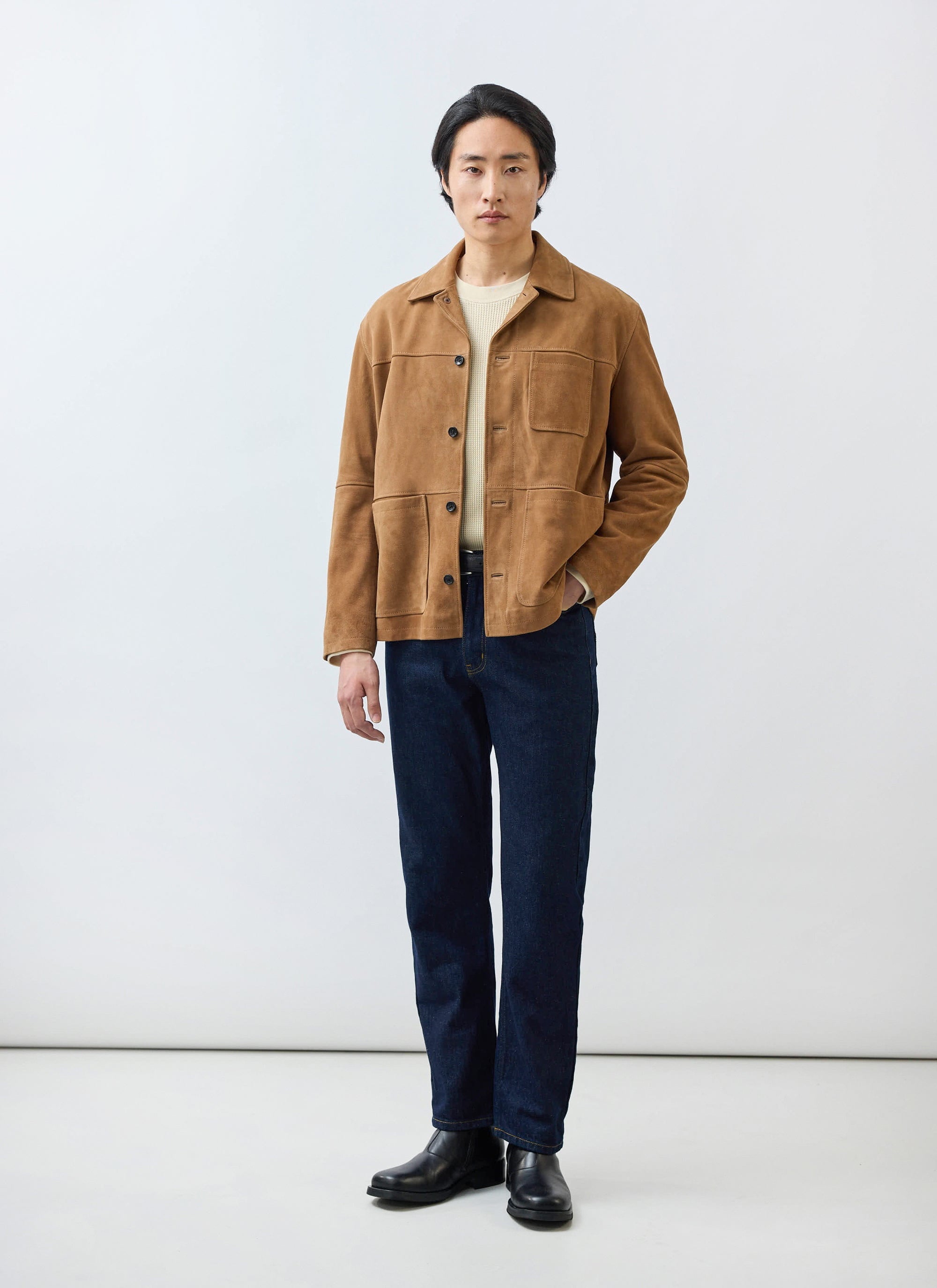 A model wears the Percival Afterward Suede Chore Jacket in tan, styled with a cream knit jumper, dark jeans, and black boots.