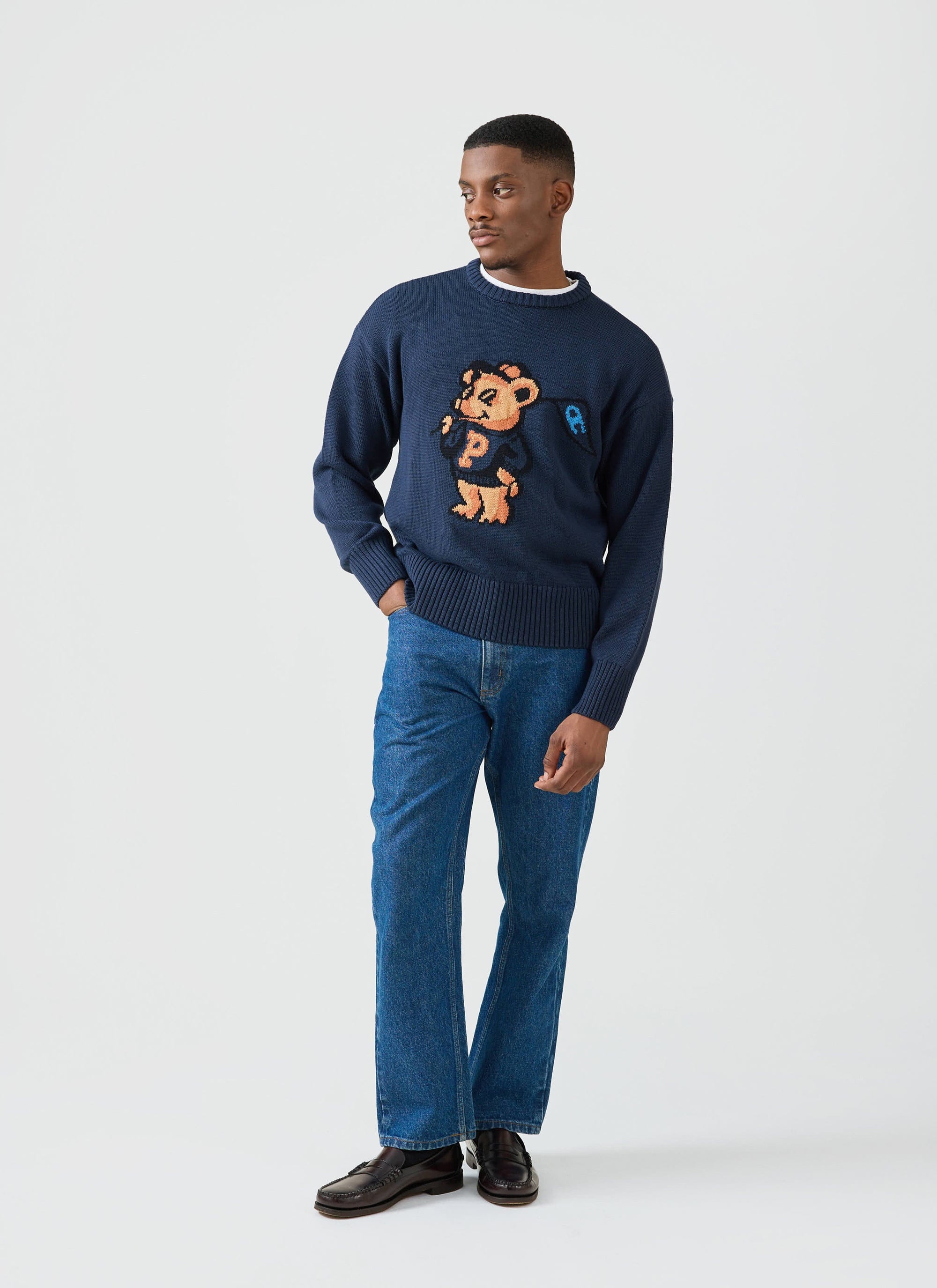 A model wears the Champion x Percival navy Jacquard Bear Crew Neck, styled with classic blue jeans and dark loafers.