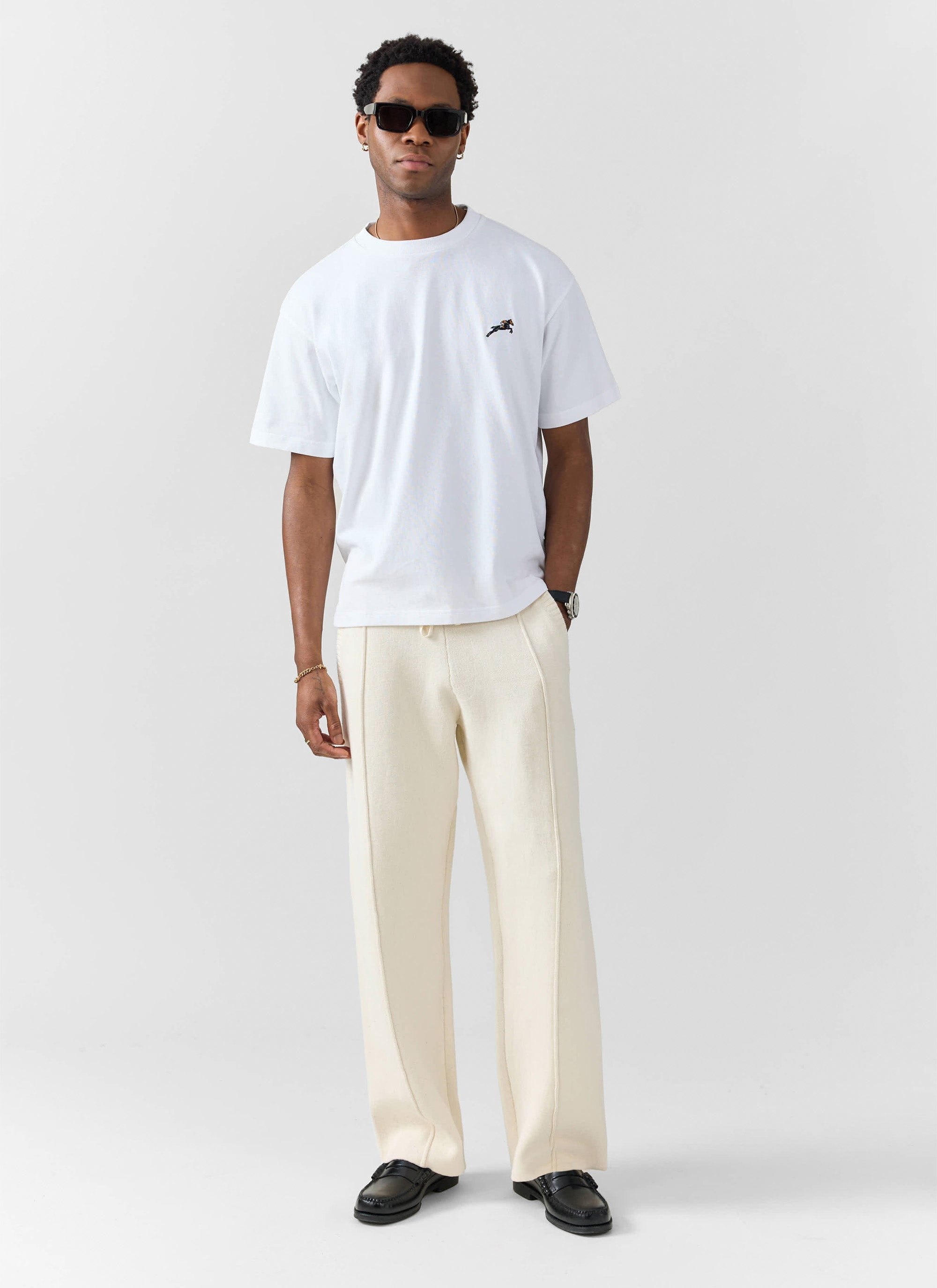 A model wears the Percival Galloping Horse embroidered t-shirt in white, styled with cream trousers and sunglasses.