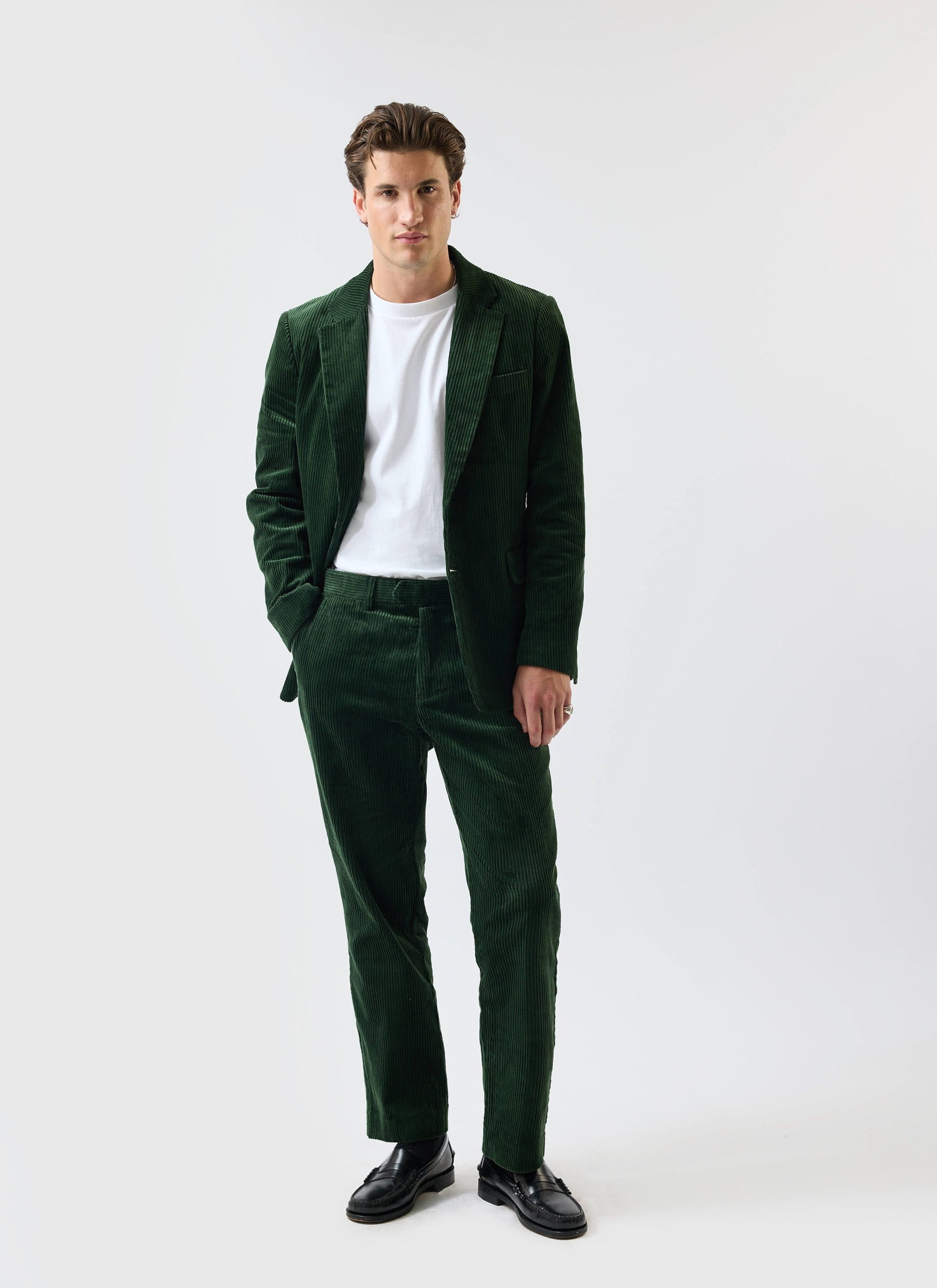 A model poses in the Percival forest green chunky cord suit, styled casually with a white t-shirt and black loafers.
