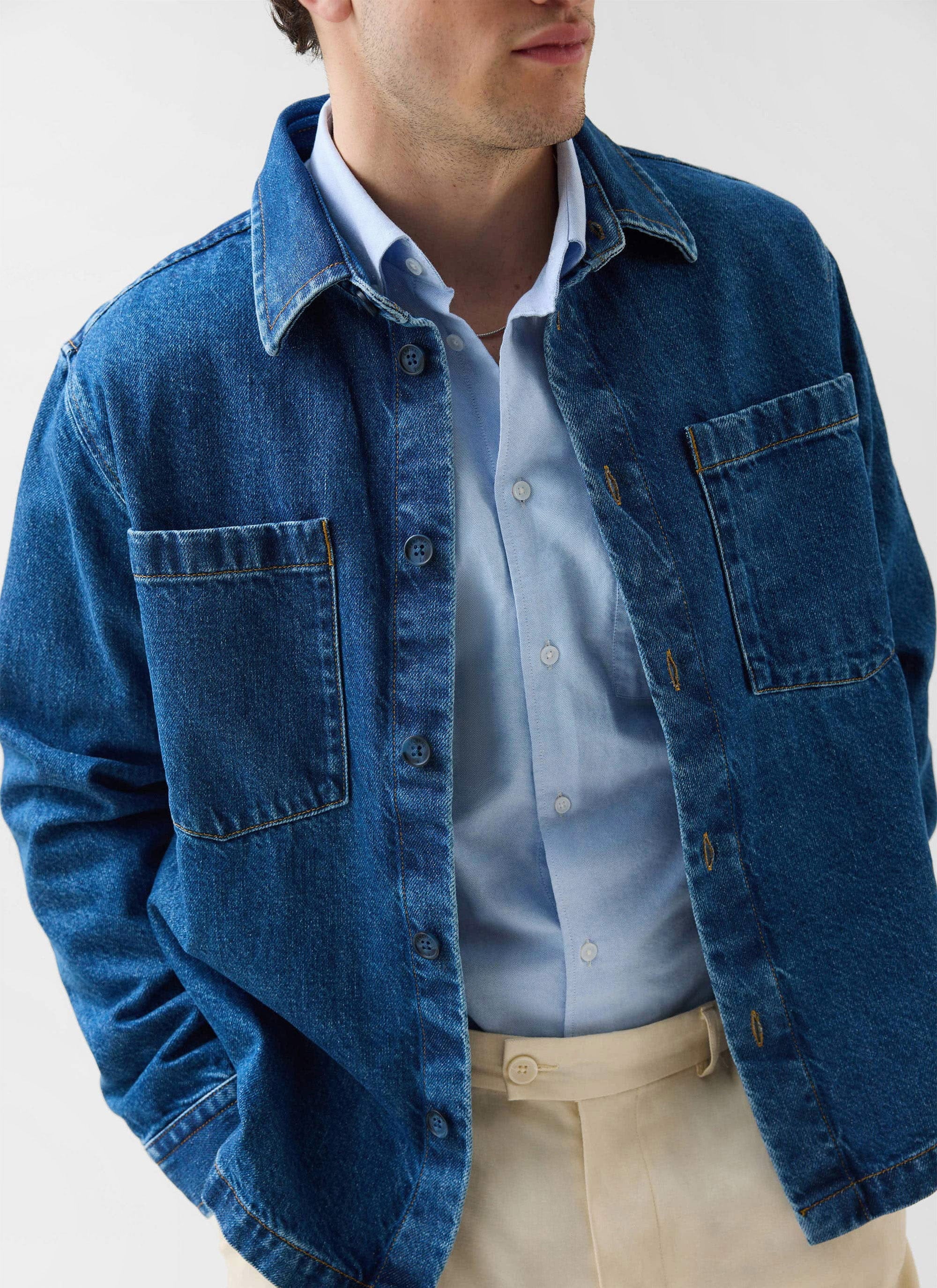 Close up of a model wearing the Percival Denim Heavyweight Overshirt in mid-wash blue layered over a light blue shirt.