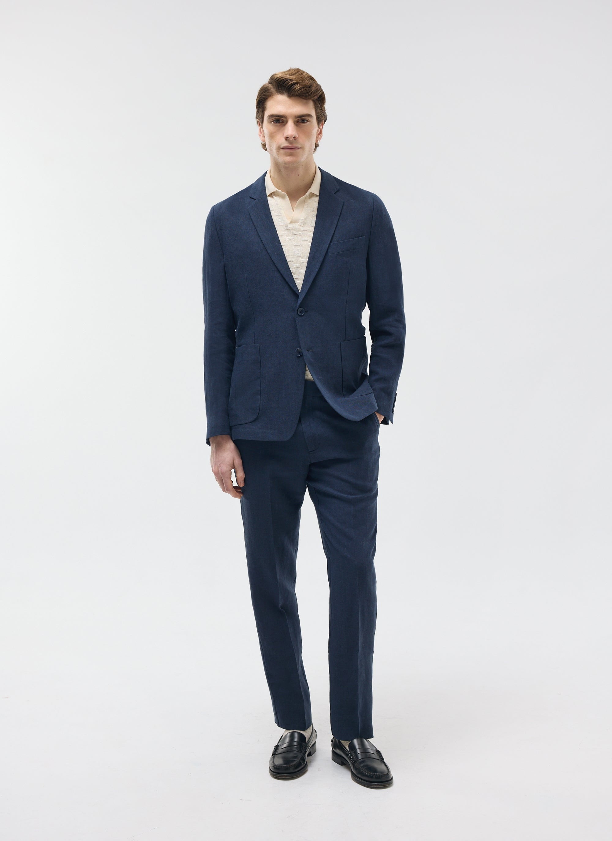 A model wears the Percival Tailored Linen Trousers in navy, styled with the matching blazer and a cream polo shirt.