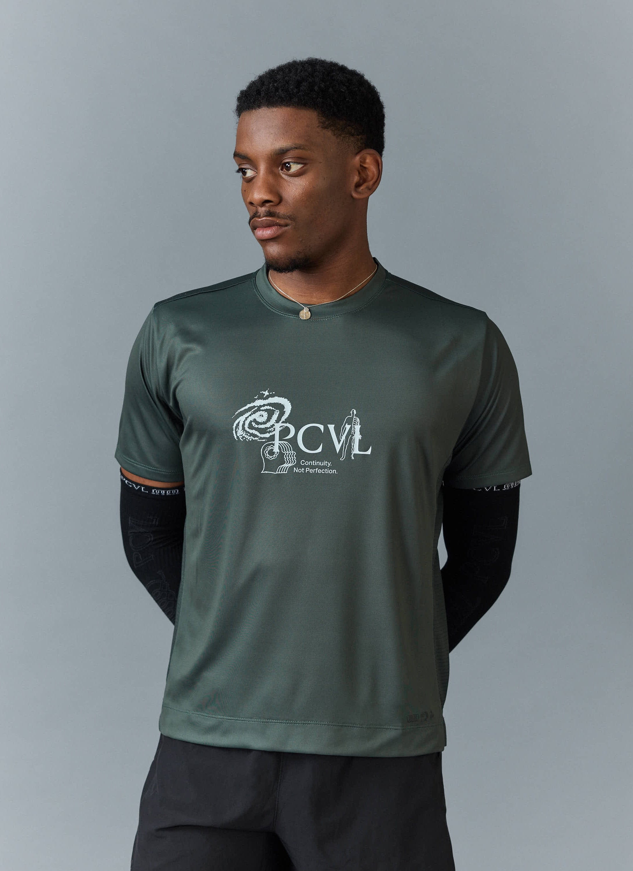 A model wears the Percival PCVL Printed Performance Top in forest green, showing the Continuity, Not Perfection chest print.