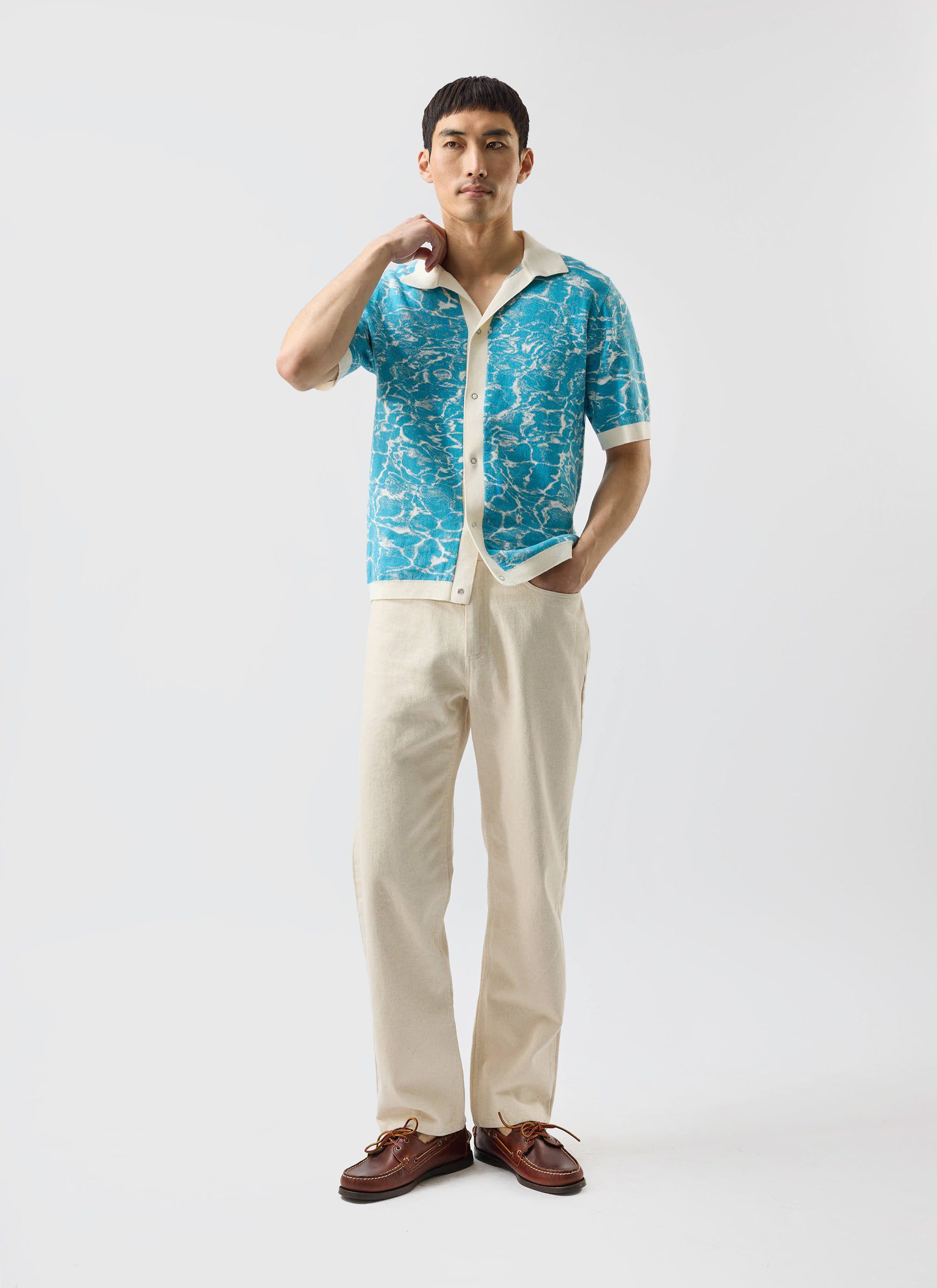 A model wears the Percival Farraris Negroni knitted shirt in a blue ocean pattern, styled with cream trousers.