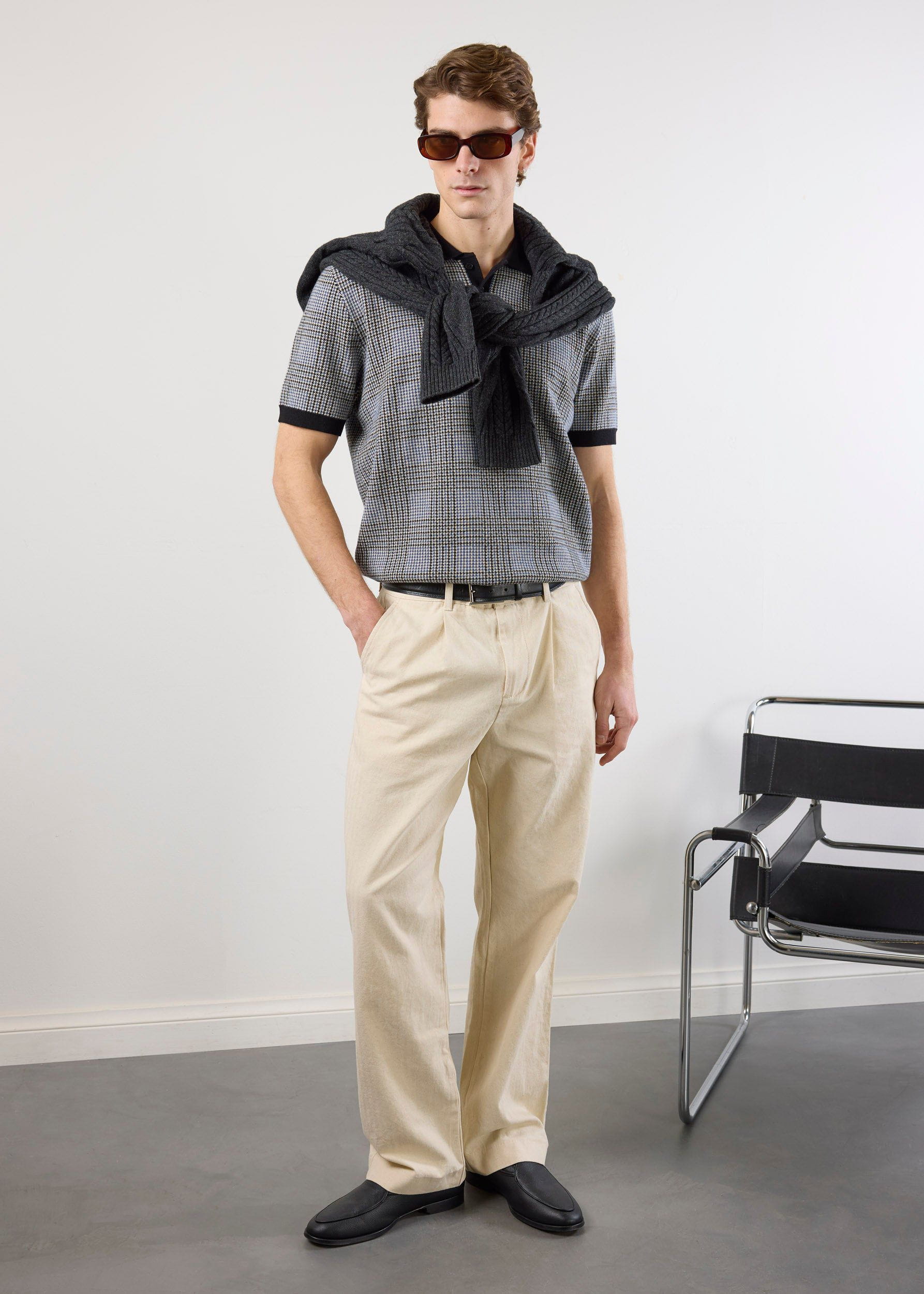 A model wears the Percival Casa Martini Knitted Polo in navy puppytooth, styled with beige trousers and a grey jumper.