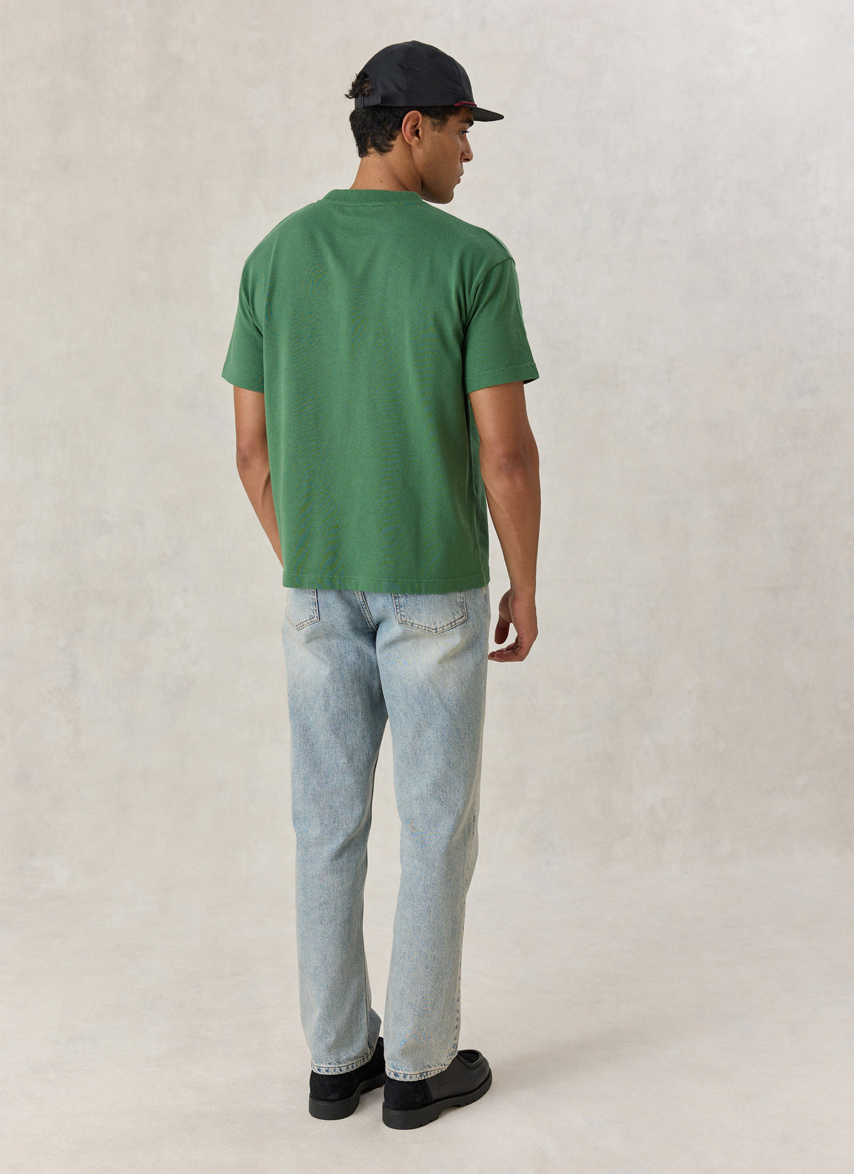 Model from the back wearing the Percival forest green organic cotton oversized t-shirt with light jeans and a black cap.
