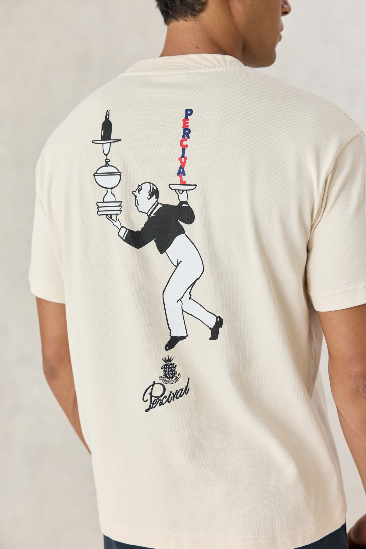 A model wearing the Percival cream Perci Waiter oversized T-shirt, showing the illustrated balancing waiter back graphic.