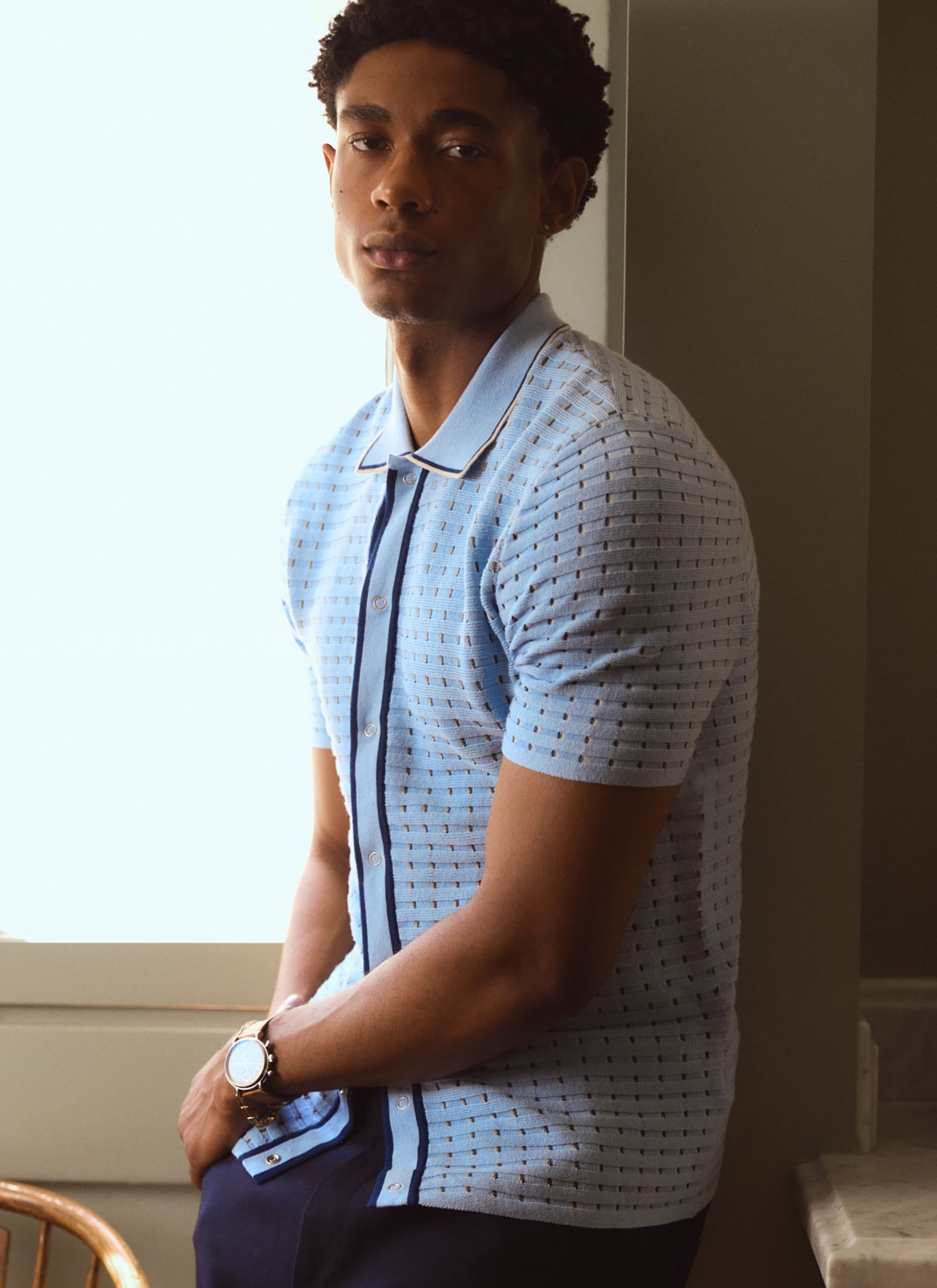 A man models the Percival Broken Stripe Knitted Shirt in light blue, a short-sleeve style with a dark blue placket.