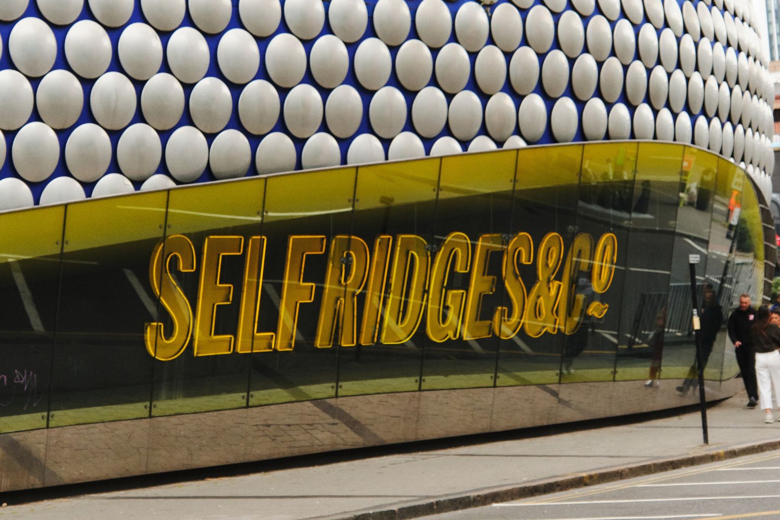 Selfridges & Co store with gold lettering against a modern building facade.