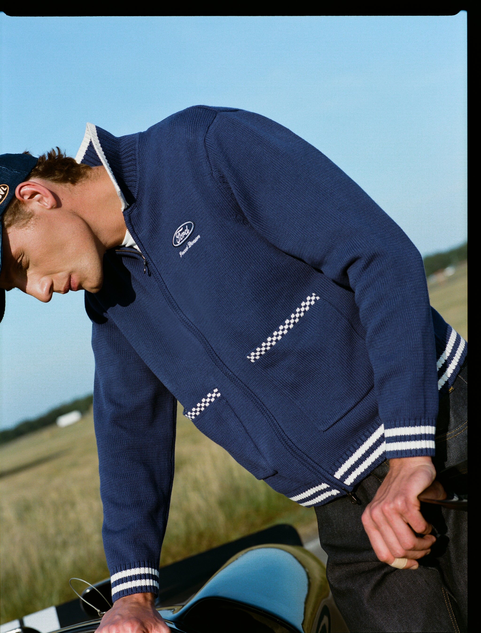 Cobalt blue Percival x Ford Gardner knitted zip cardigan, styled with dark heritage denim jeans in a racing setting.