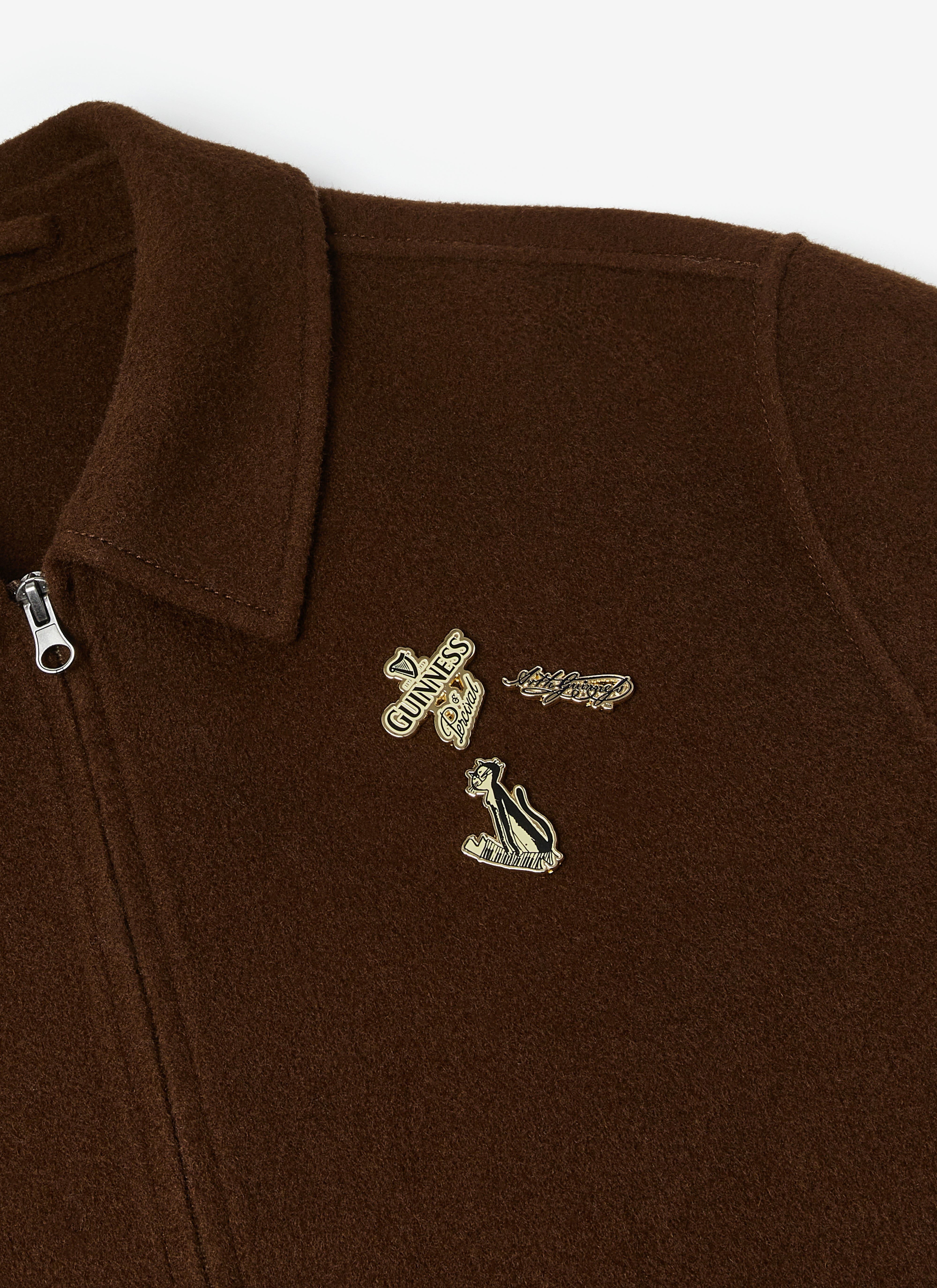 A close-up of the collaboration pins on the chest of the espresso brown Guinness x Percival wool jacket.