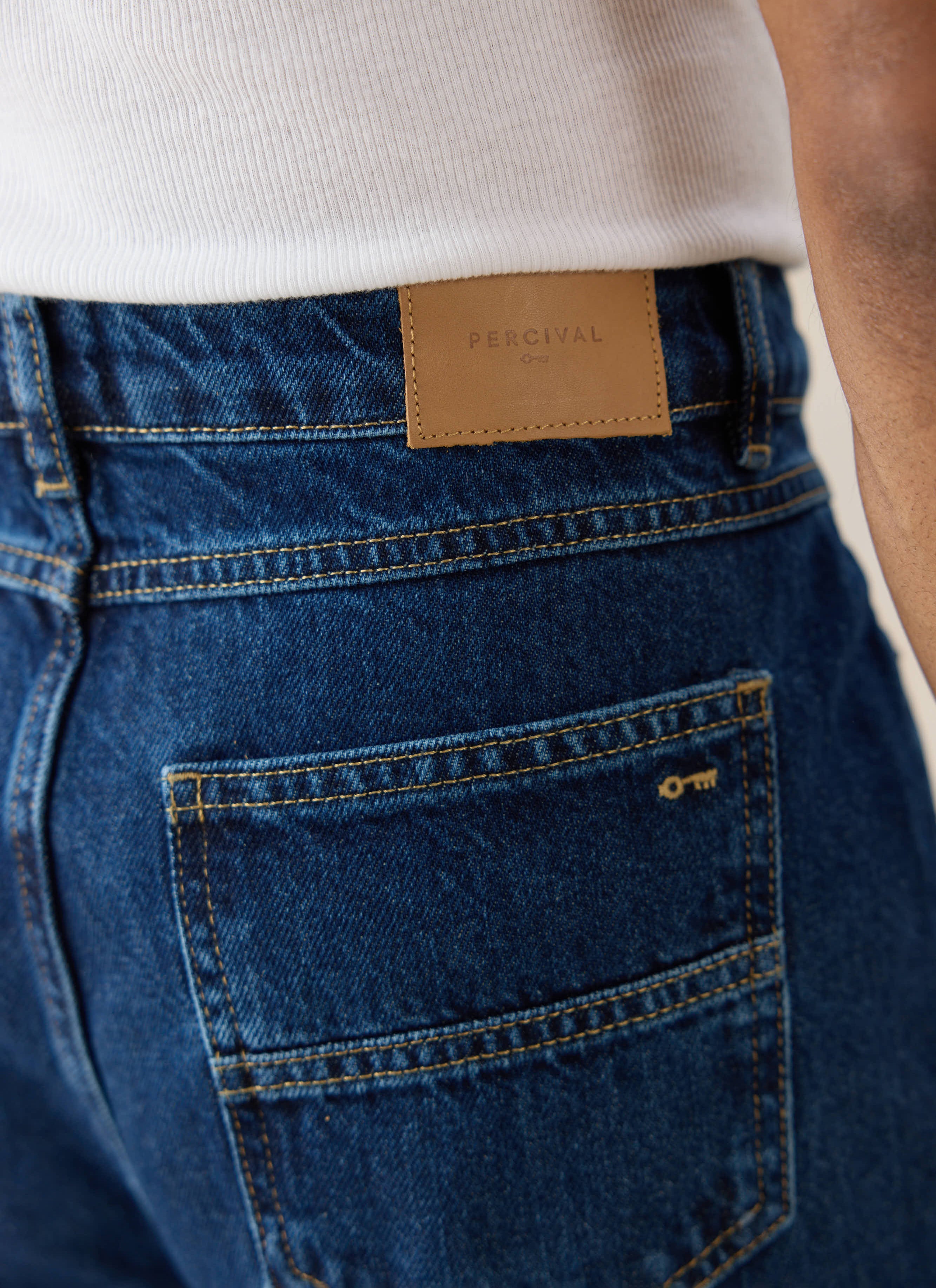 Percival mid wash 12oz pleated denim jeans, showing the leather brand patch and signature contrast-stitched back pocket.