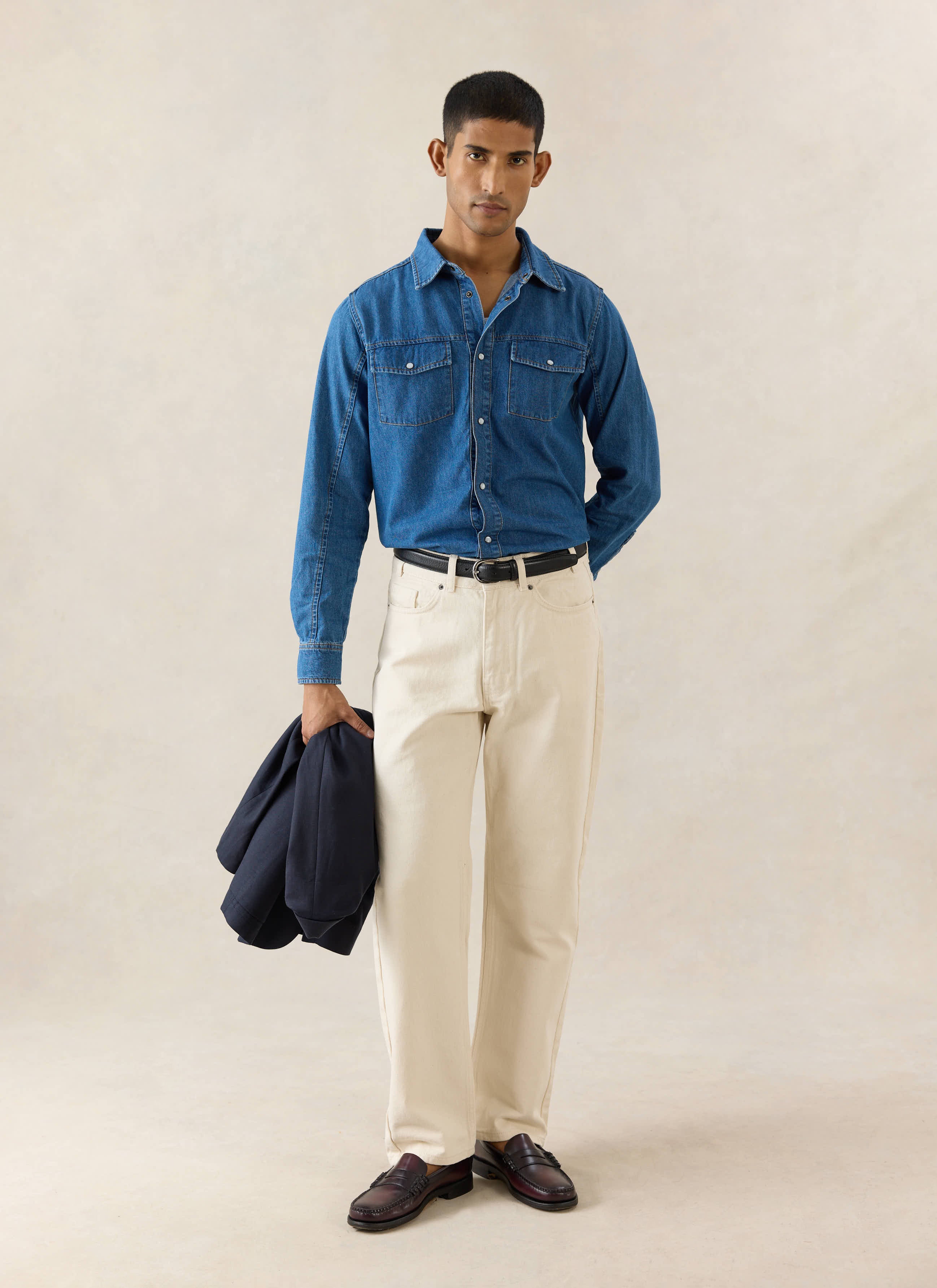 Mid wash blue Percival denim western shirt with pearl buttons, styled tucked into cream trousers on a model.