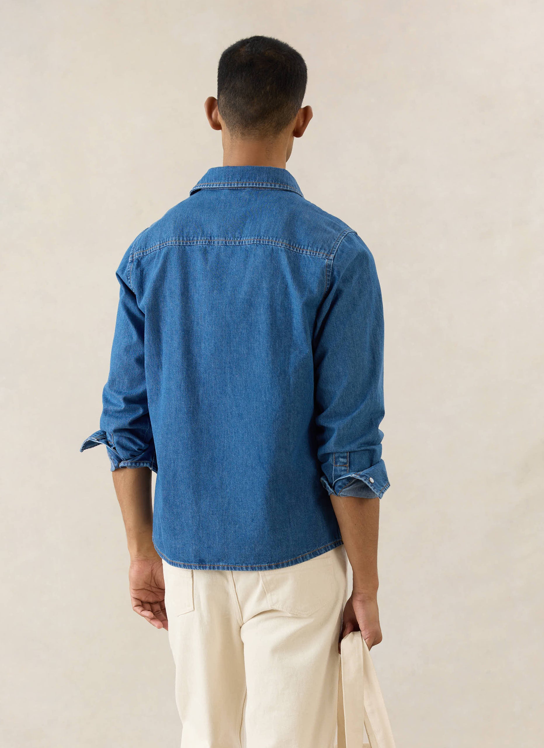 The Percival Vintage Wash Western Shirt in mid wash blue denim, seen from behind on a model with rolled sleeves.