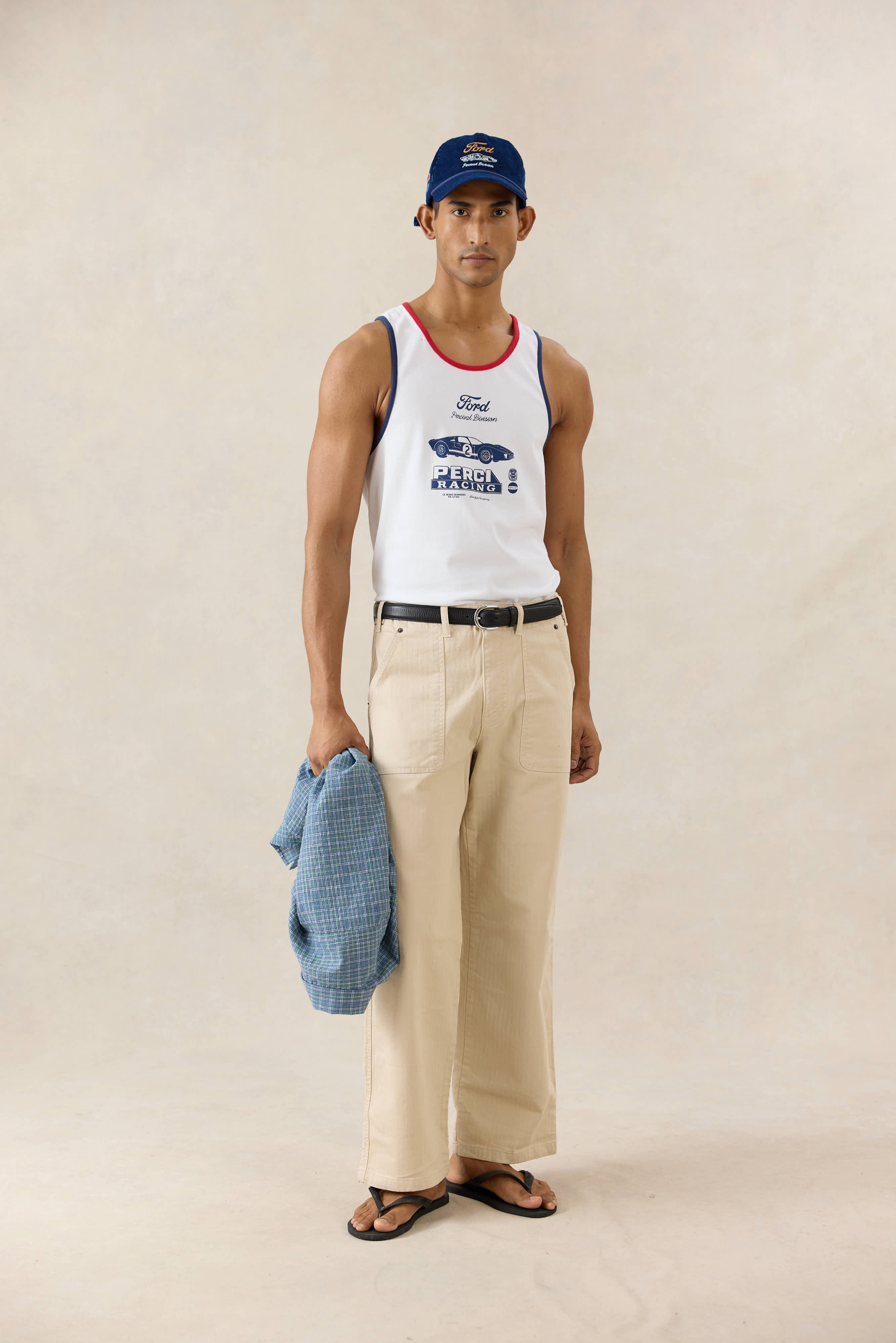 A model wears the white Ford x Percival GT40 ringer vest with red trim, styled with cream trousers and a navy cap.