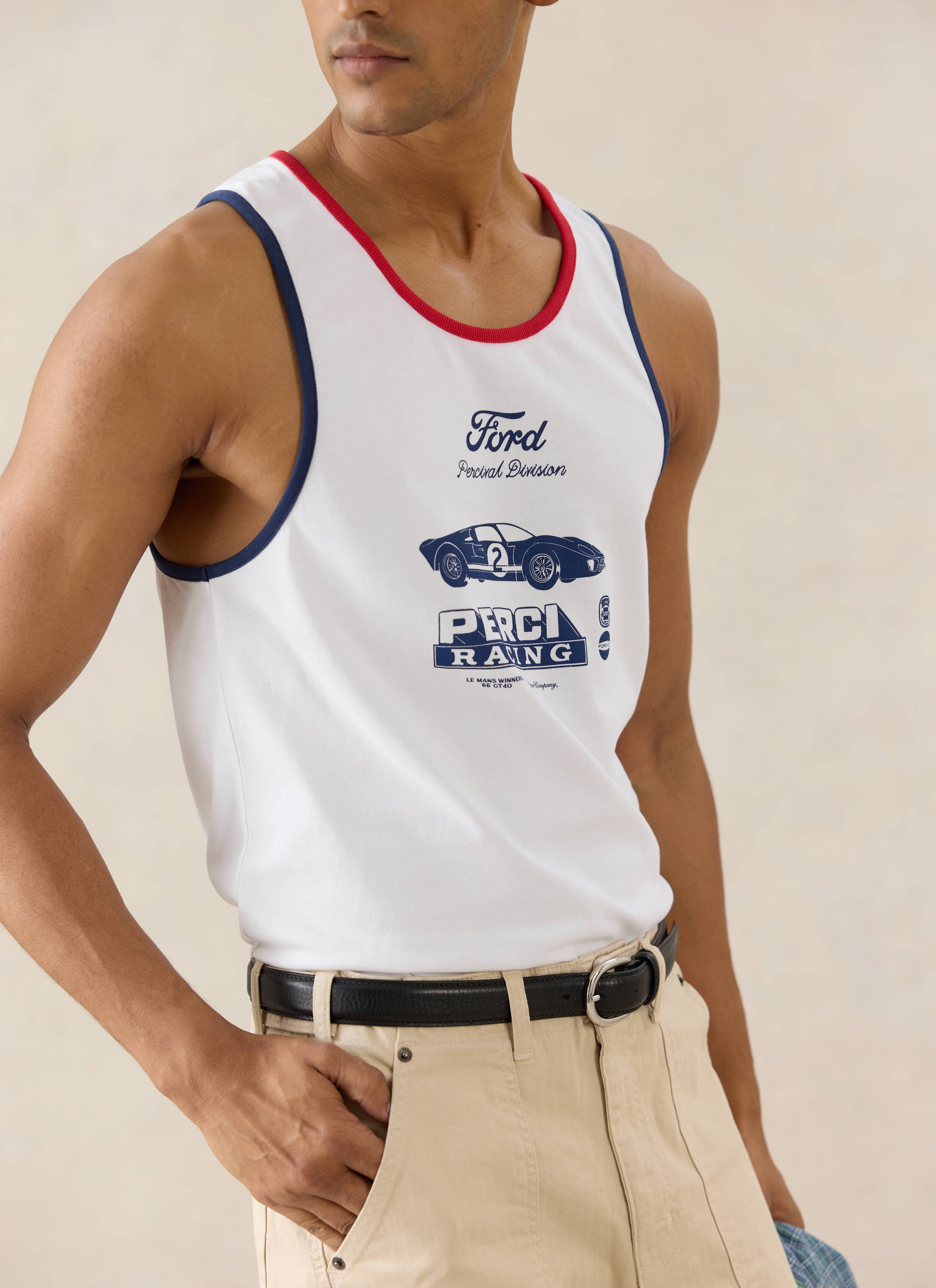 A model wears the white organic cotton Ford x Percival GT40 Ringer Vest, styled with beige trousers and a black belt.