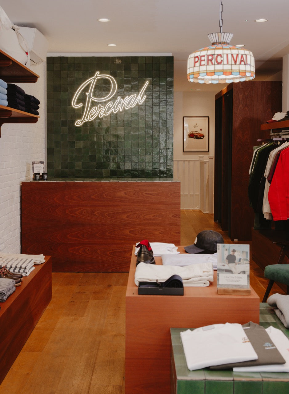 Inside a Percival store featuring a neon logo on a green tiled wall and a framed print in the background.