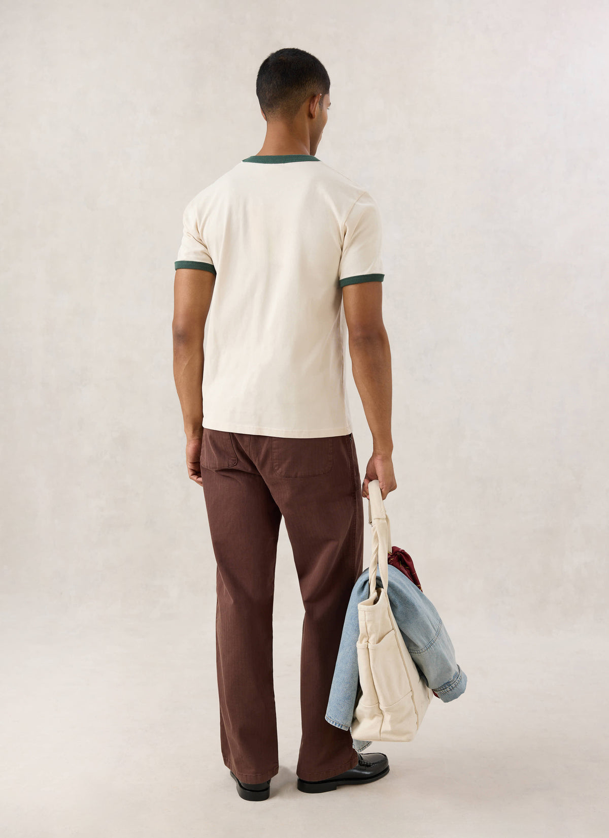 Rear view of a model wearing the cream Guinness x Percival ringer T-shirt with forest green trim.