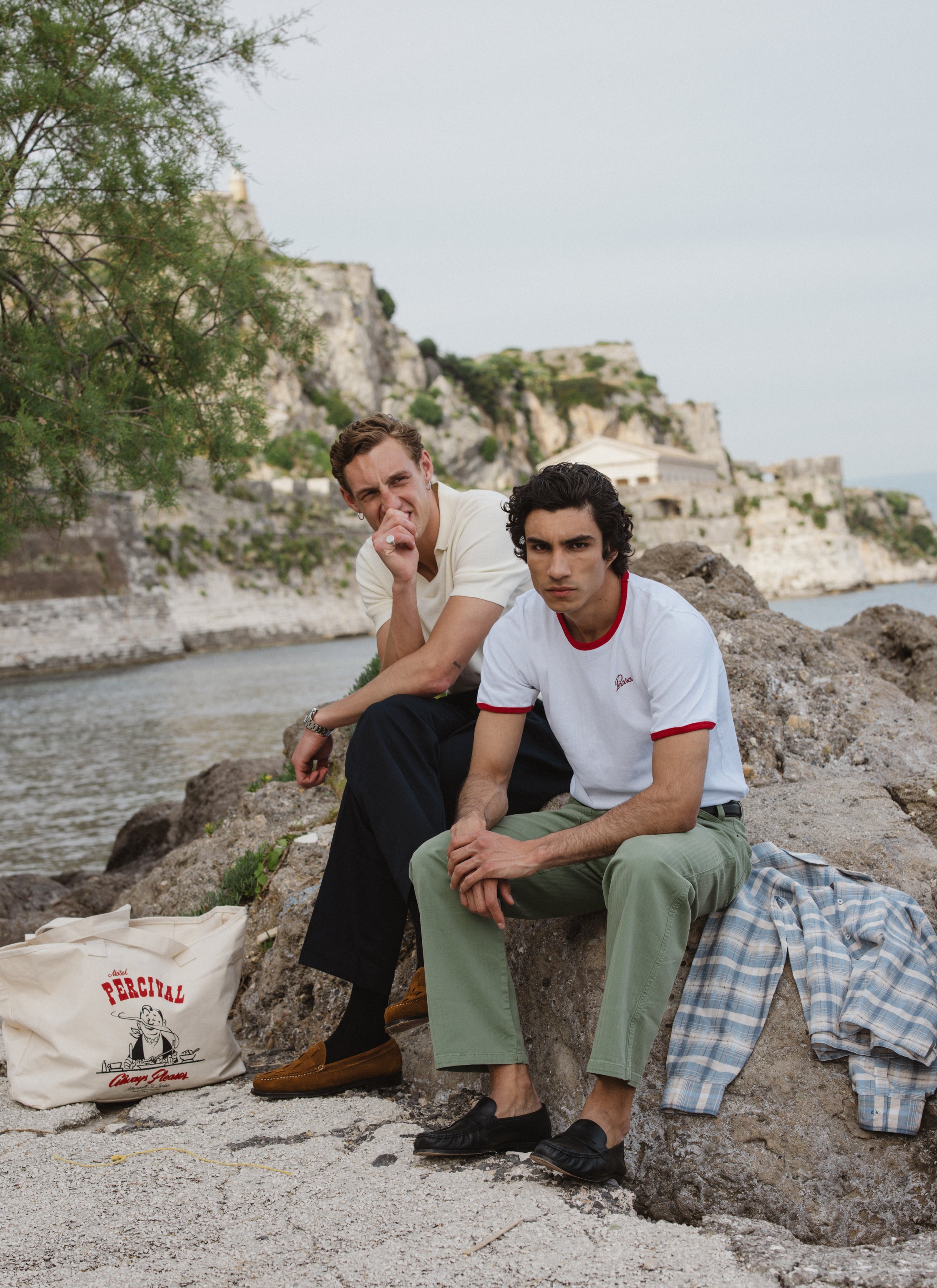 Percival white ringer t-shirt and sage trousers on a model by the sea; check out the full SS26 collection.
