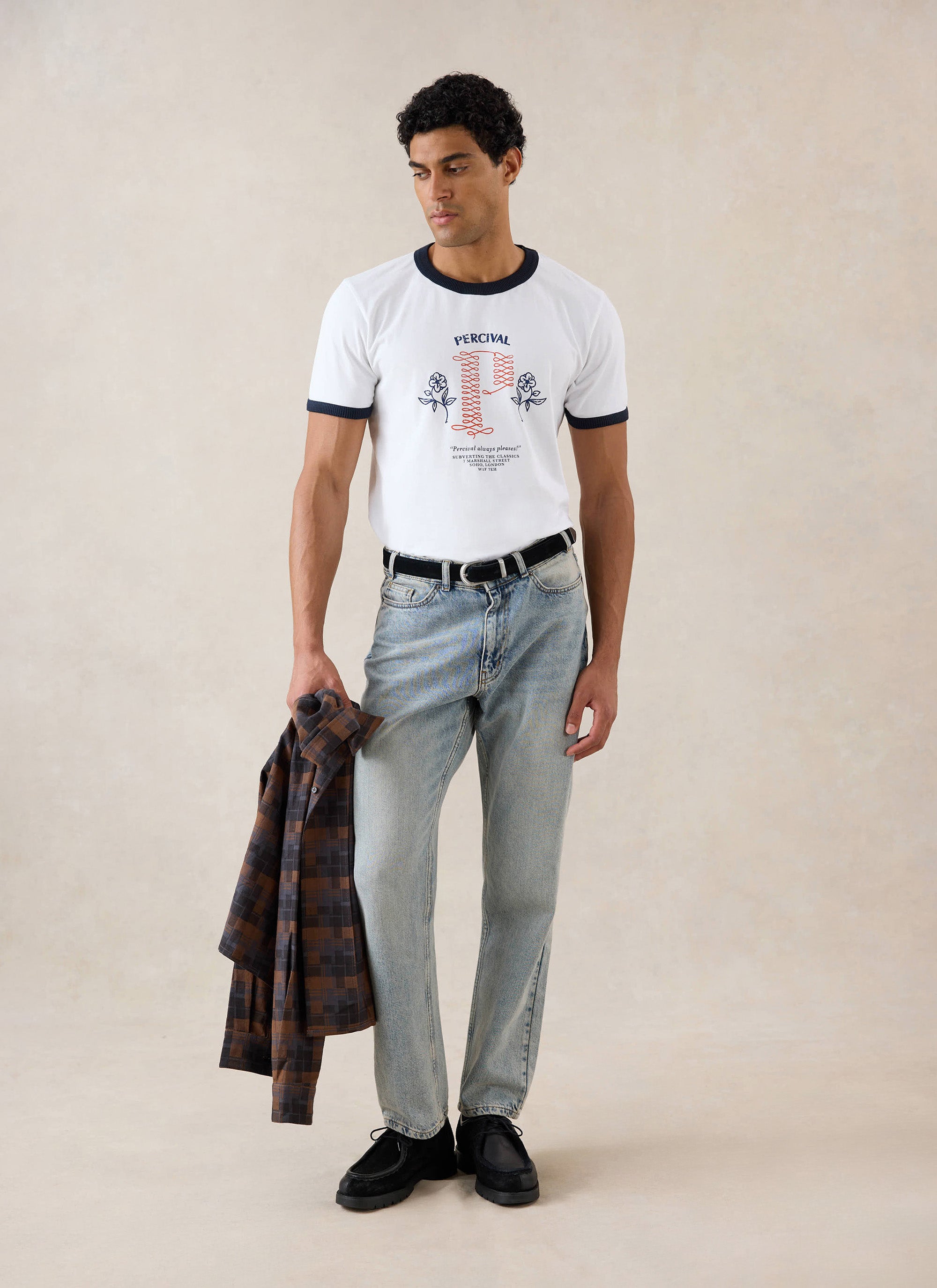 A model wears the white Percival Tucker ringer T-shirt with graphic embroidery, styled with light wash jeans.