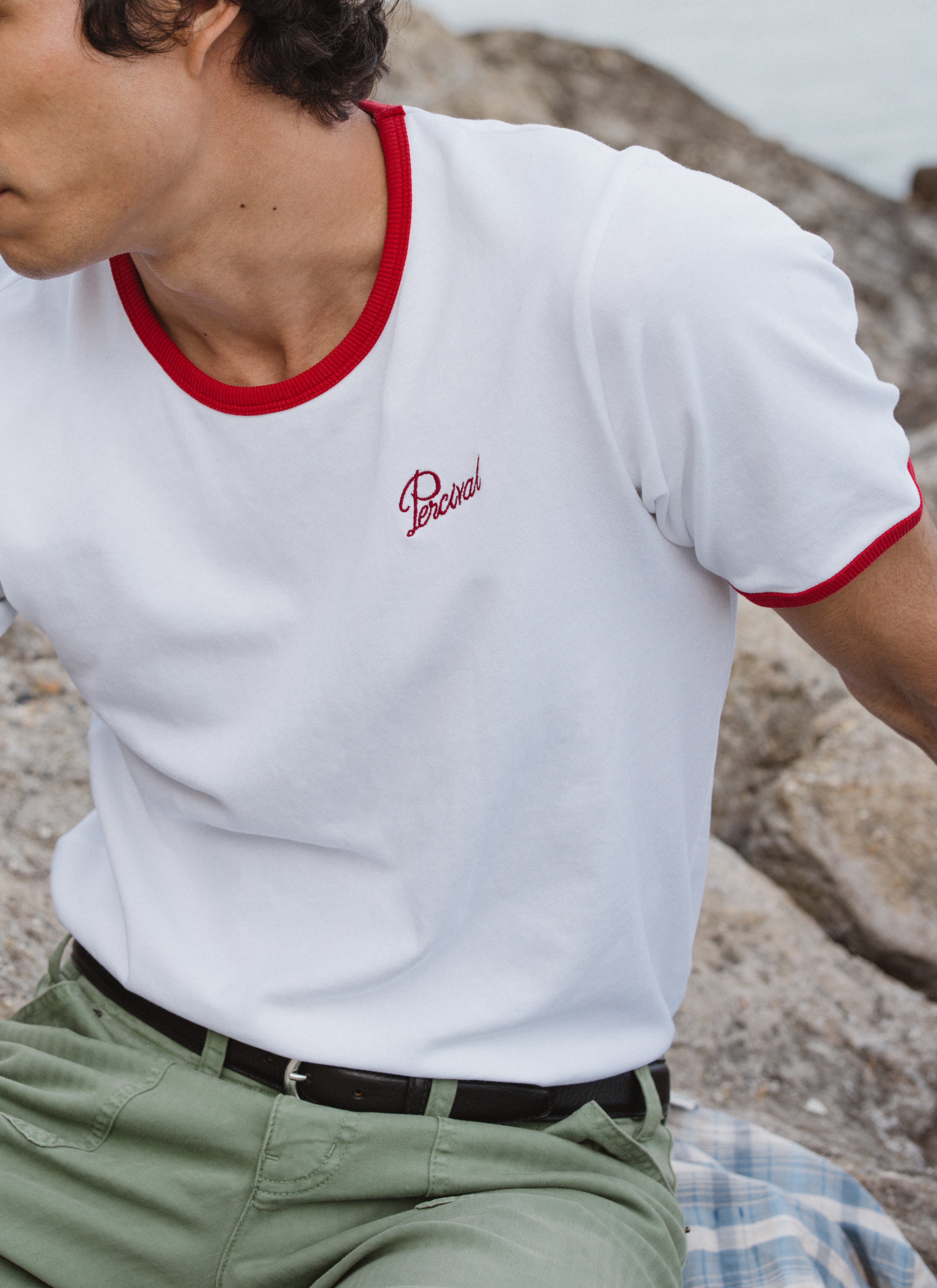 White Percival organic cotton ringer t-shirt with red trim and chest logo, worn by a model in a rocky setting.