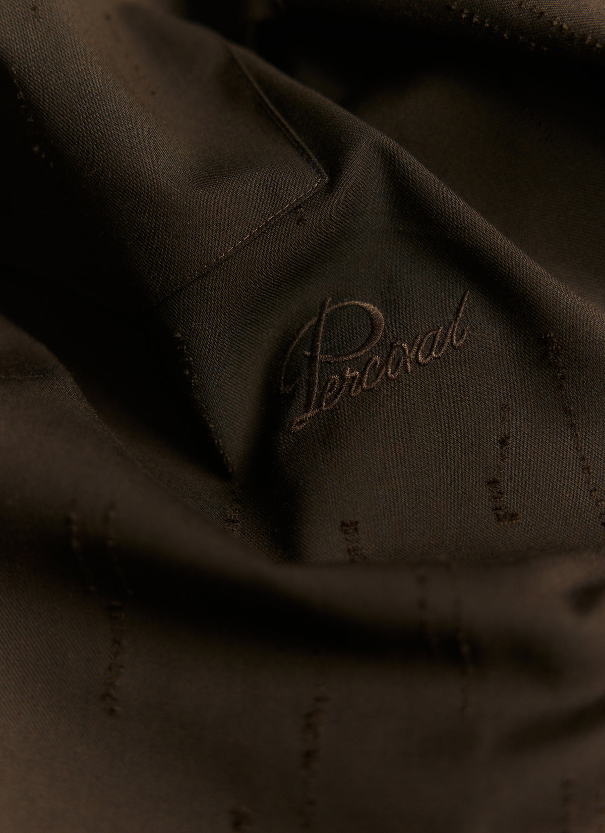 Close-up of espresso brown Percival Rowley jacquard shirt showing the tonal embroidered logo and fabric detail.