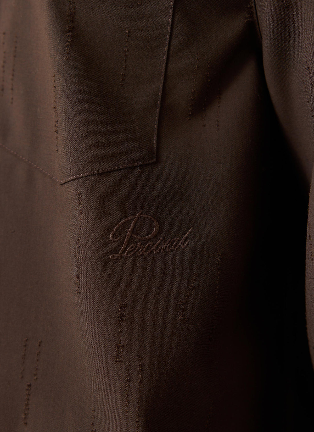 Close-up of espresso brown Percival Rowley textured jacquard shirt, showing the chest pocket and tonal embroidered logo.
