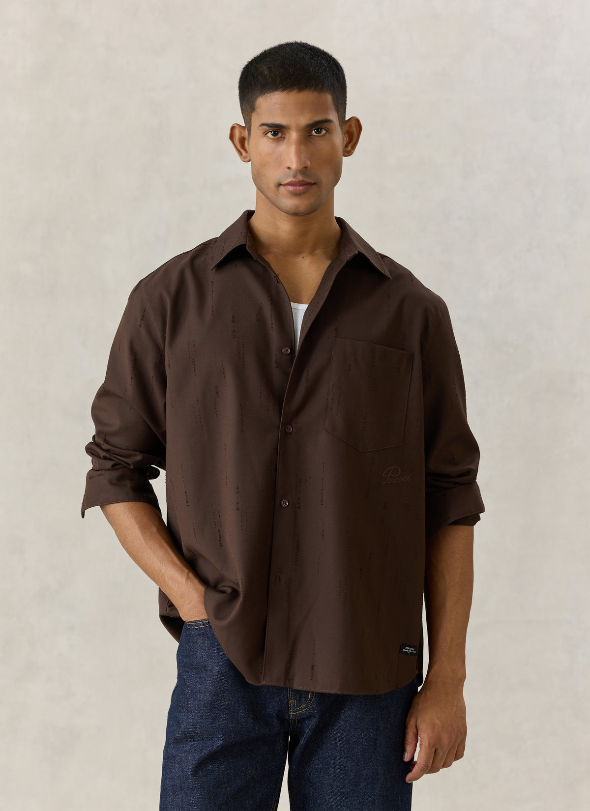 A model wearing the Percival Rowley textured jacquard shirt in espresso brown with a chest pocket, styled with blue jeans.