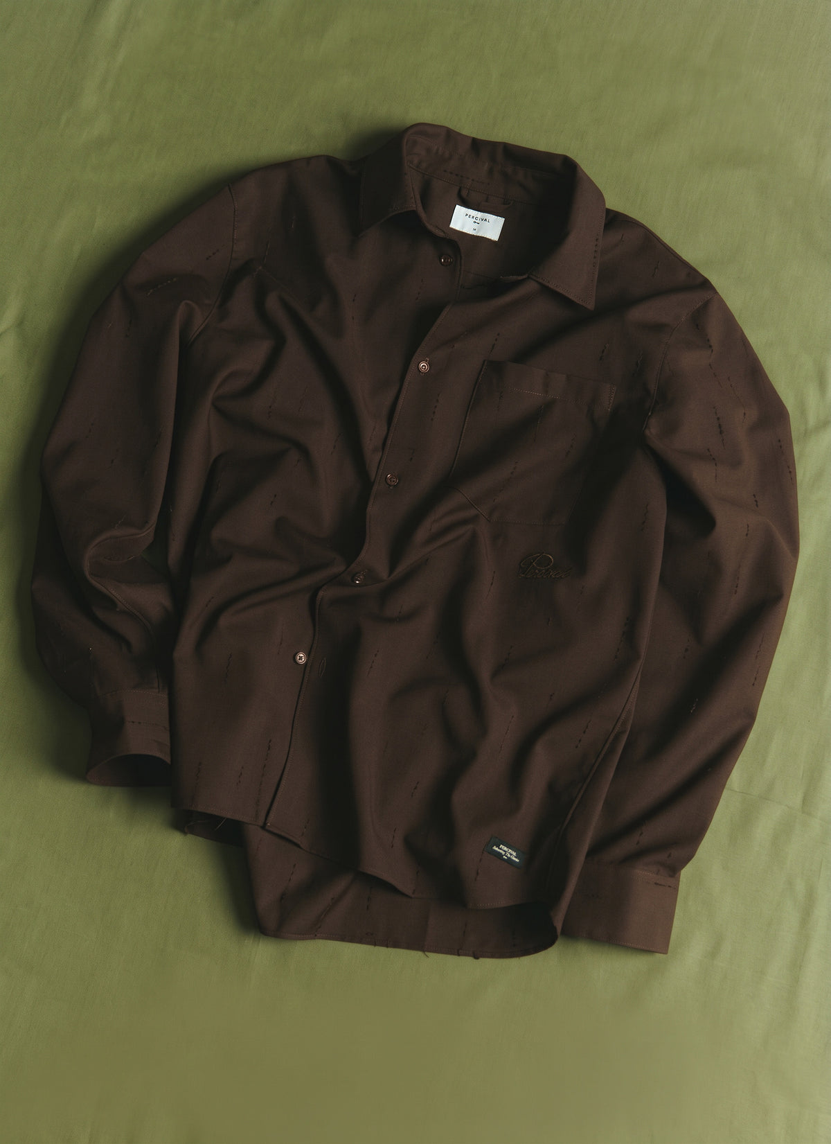 The Percival espresso brown Rowley textured jacquard shirt laid flat on a green surface.