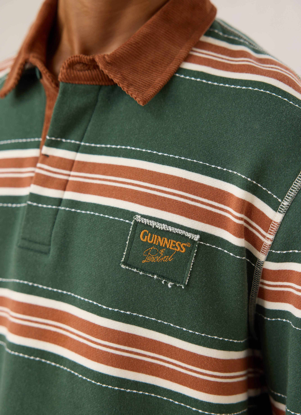 Close-up of the Guinness x Percival striped rugby shirt in green, showing the brown cord collar and chest patch.