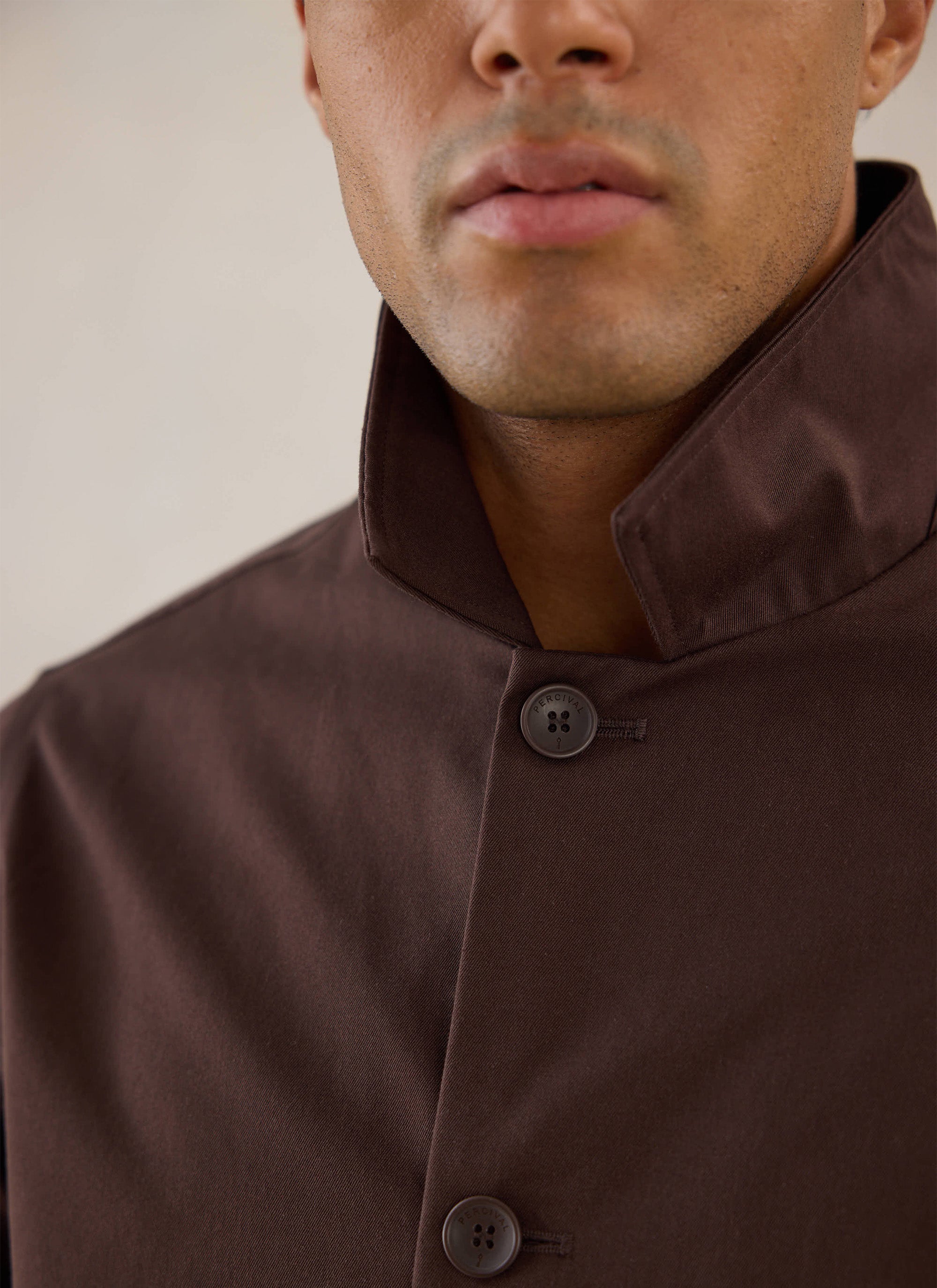 Model wearing the espresso brown Percival Sherlock short trench coat, showing the high collar and button details.