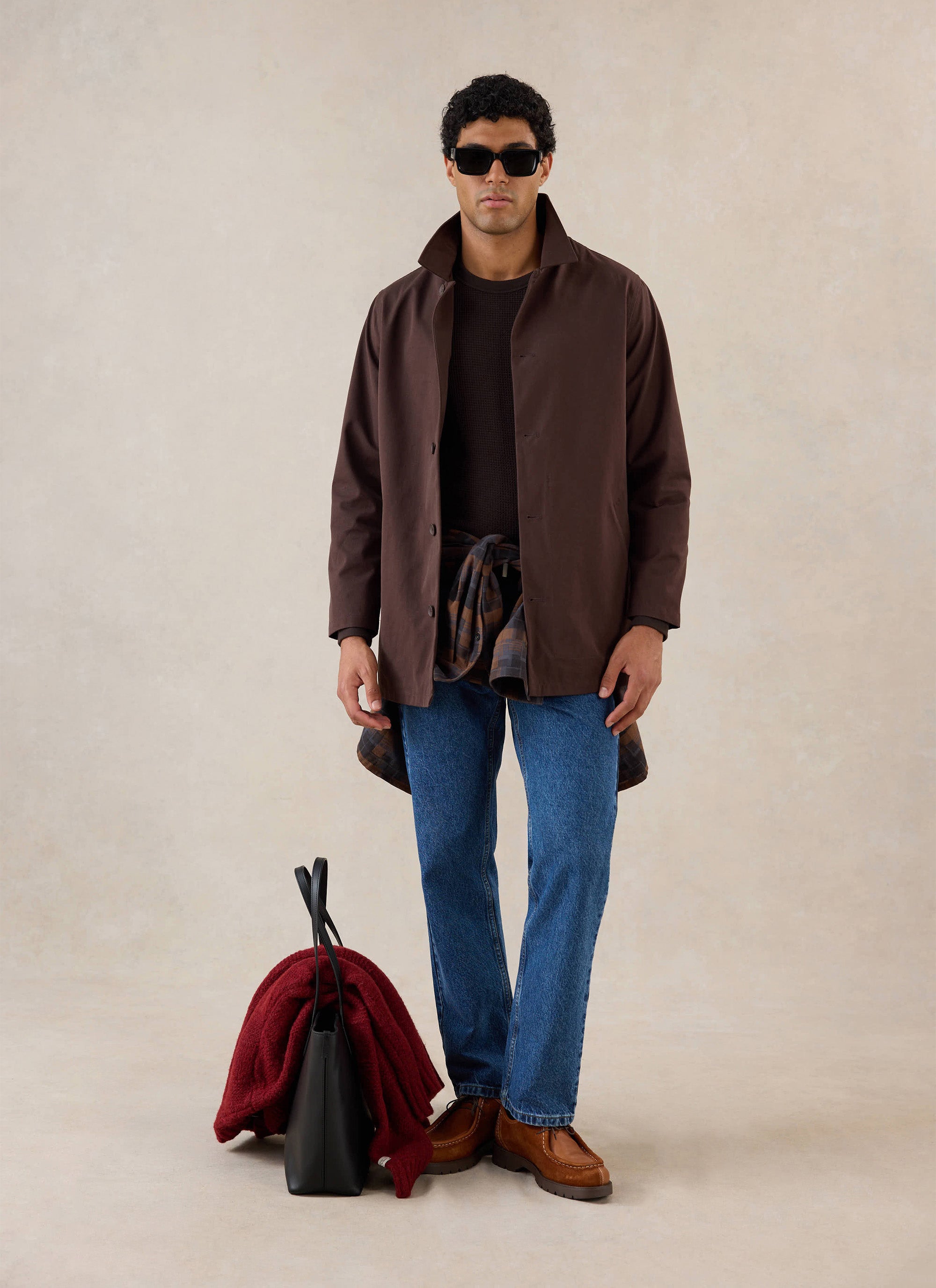A model wears the Percival espresso brown Sherlock short trench coat with blue jeans and sunglasses.