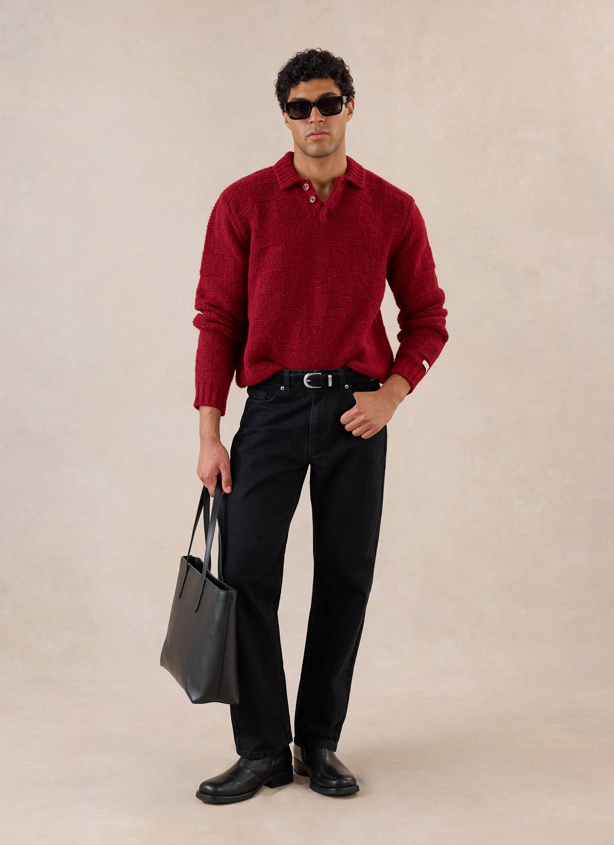 A model wears the merlot Percival Shugart boxy knit jumper, styled with black trousers and a black tote bag in a studio shot.