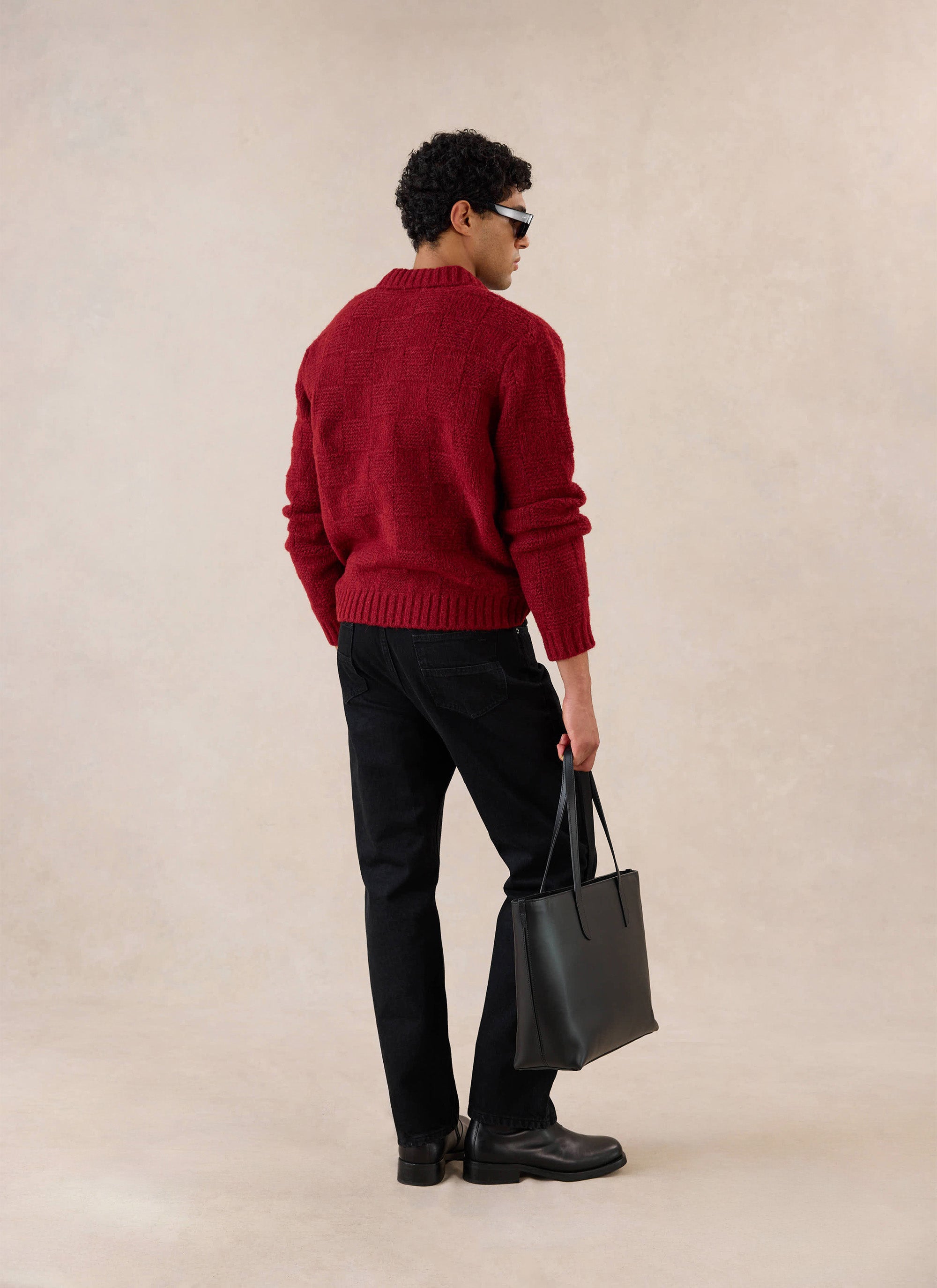 A model seen from behind wears the merlot Percival Shugart Knit Jumper, styled with black trousers and a black tote bag.