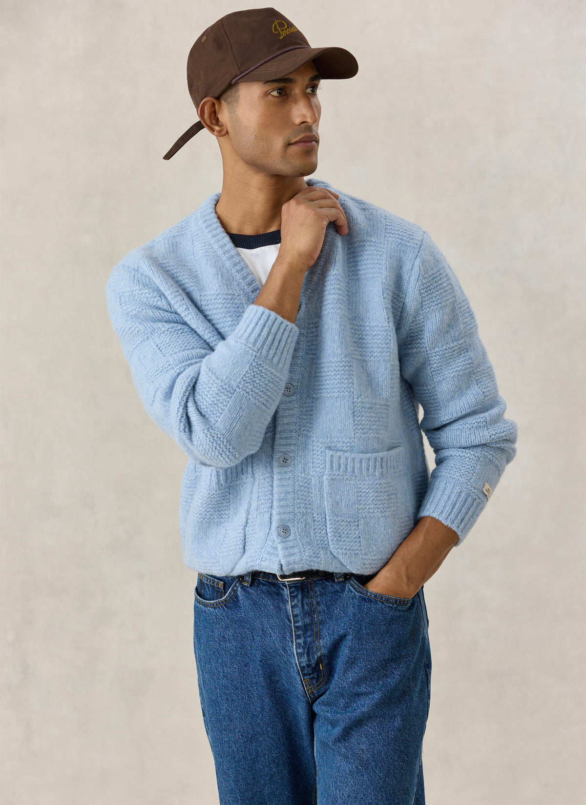 A model wearing the light blue Percival Shugart knit cardigan in alpaca wool blend with jeans and a brown cap.