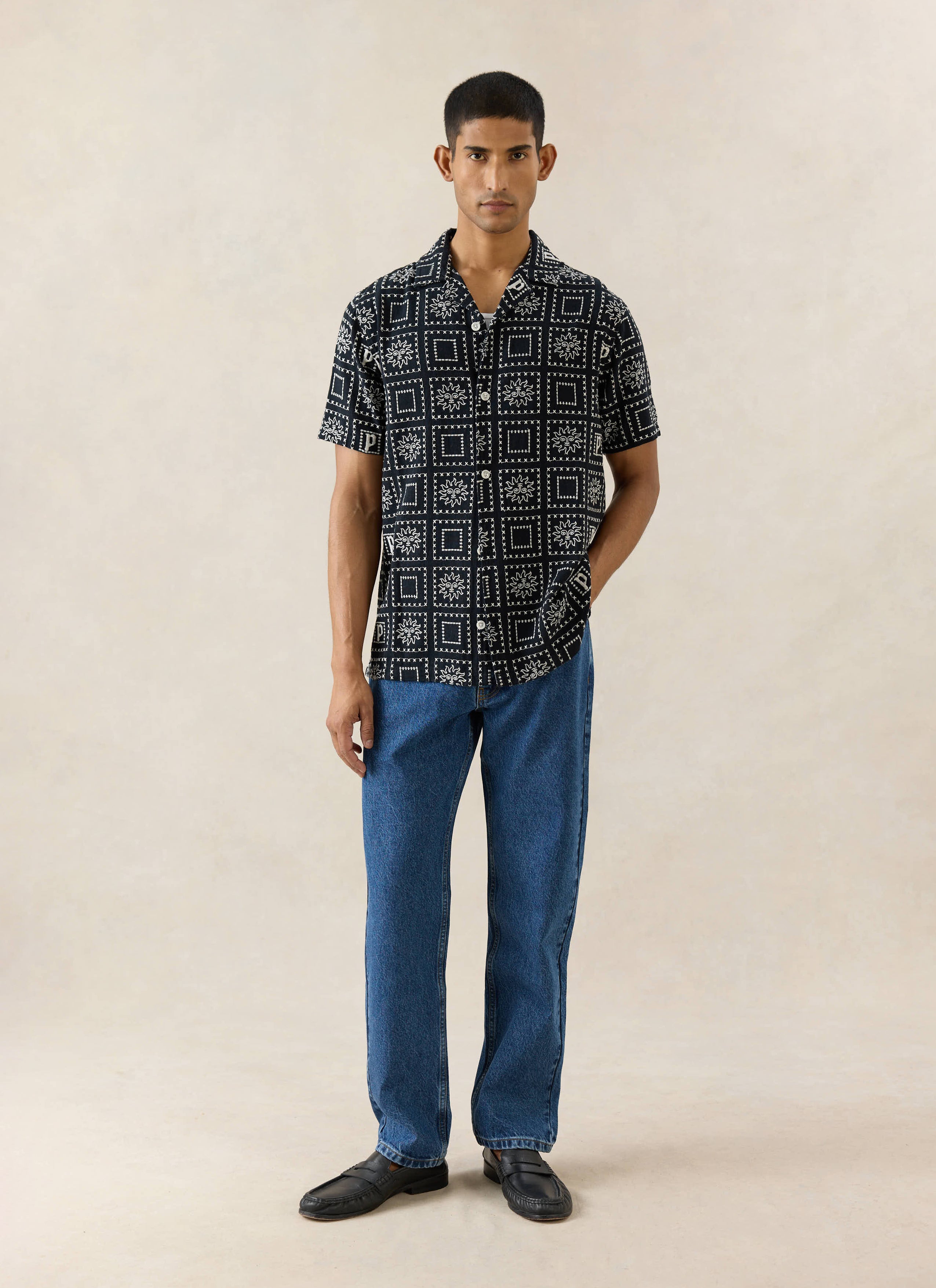 Percival Solis Heaton Cuban shirt in black linen blend with white sun patterns, styled with jeans and loafers.
