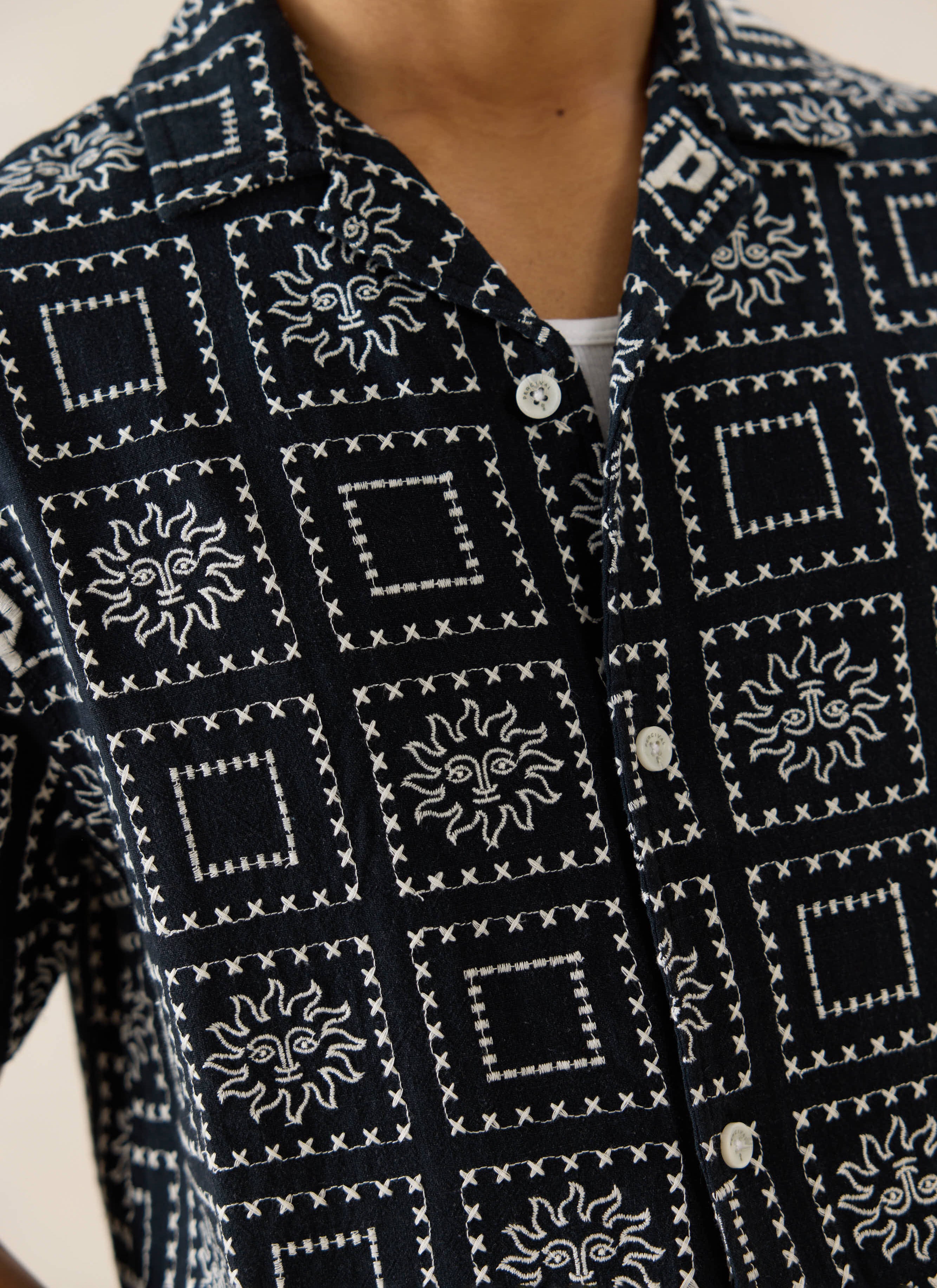 The black linen-blend Percival Solis Heaton Cuban Shirt in a close-up, highlighting white sun and square embroidery.