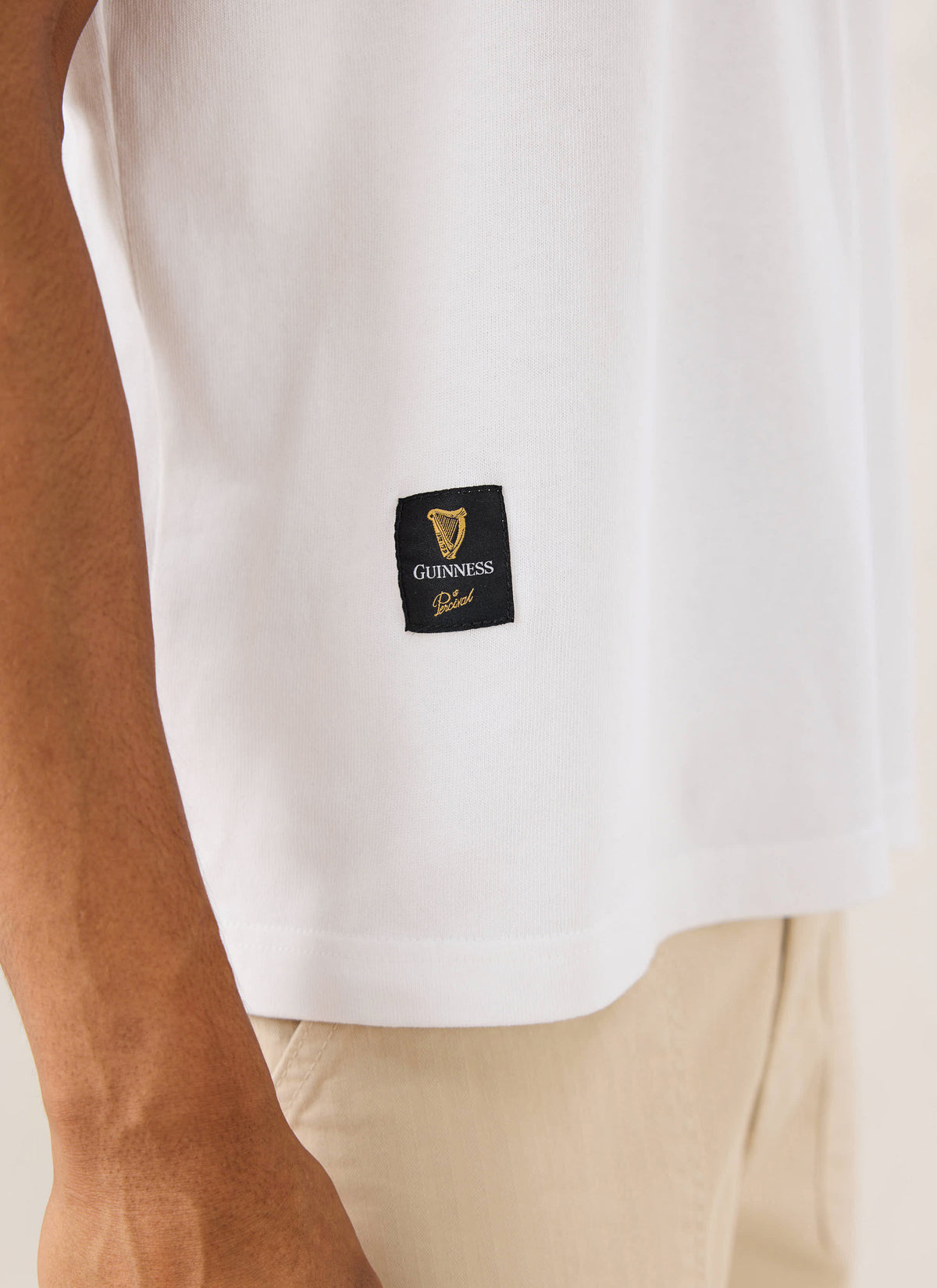 A close-up of the white Guinness x Percival T-shirt, highlighting the woven co-branded label stitched at the hem.