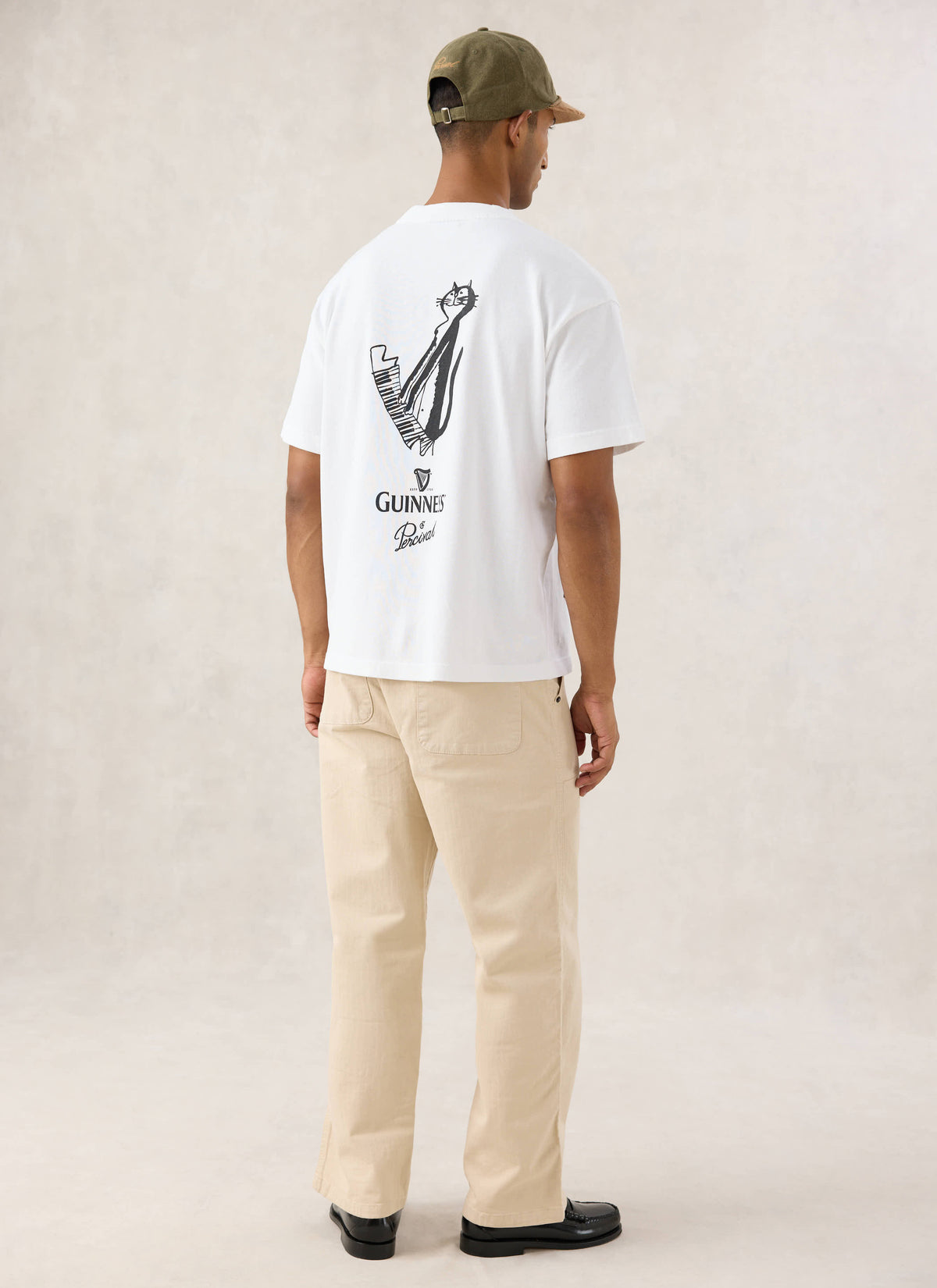 Rear view of a model wearing the white Guinness x Percival oversized T-shirt with the cat playing piano back graphic.