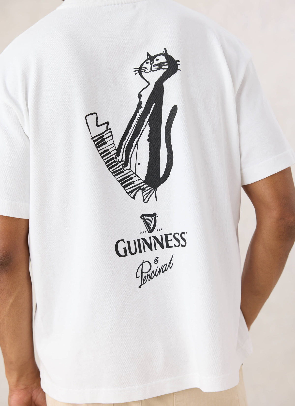 Rear view of a model wearing the white Guinness x Percival Soloist T-shirt featuring the cat playing piano back print.