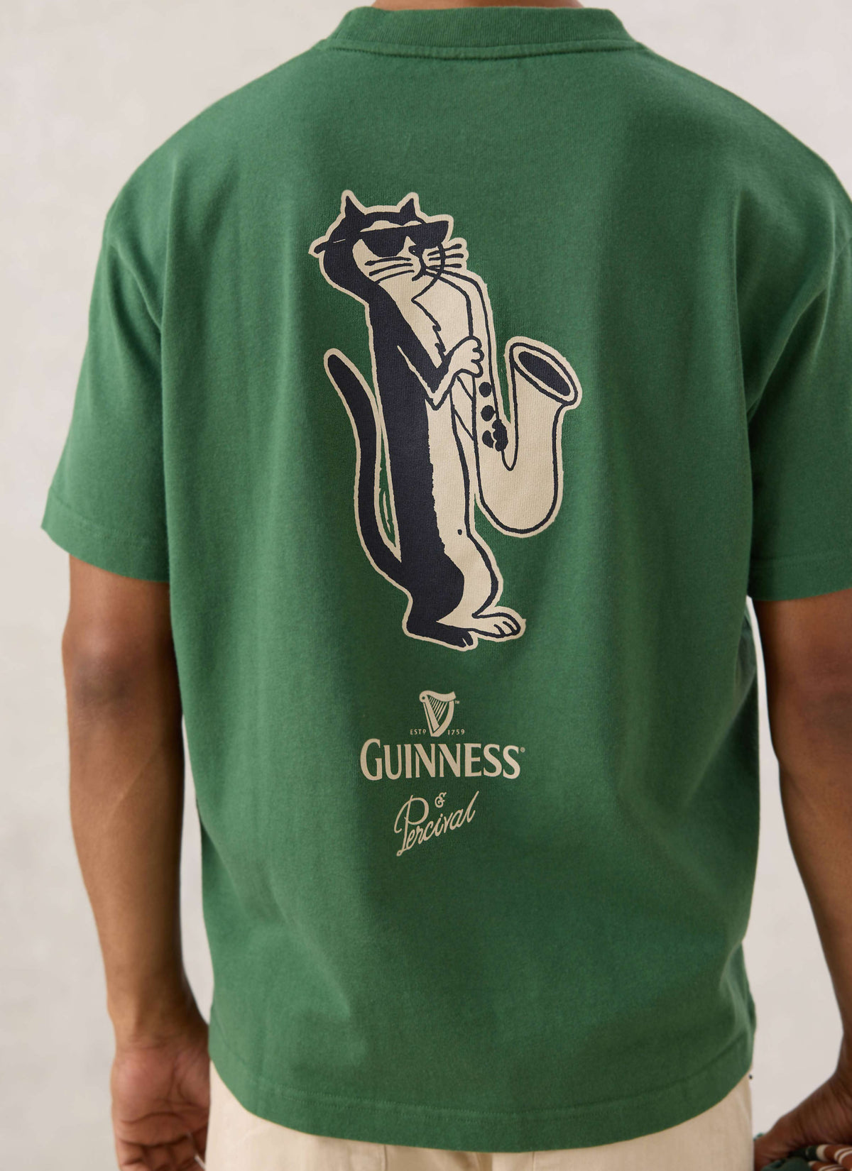 Rear view of a model wearing the forest green Guinness x Percival saxophonist cat oversized T-shirt.