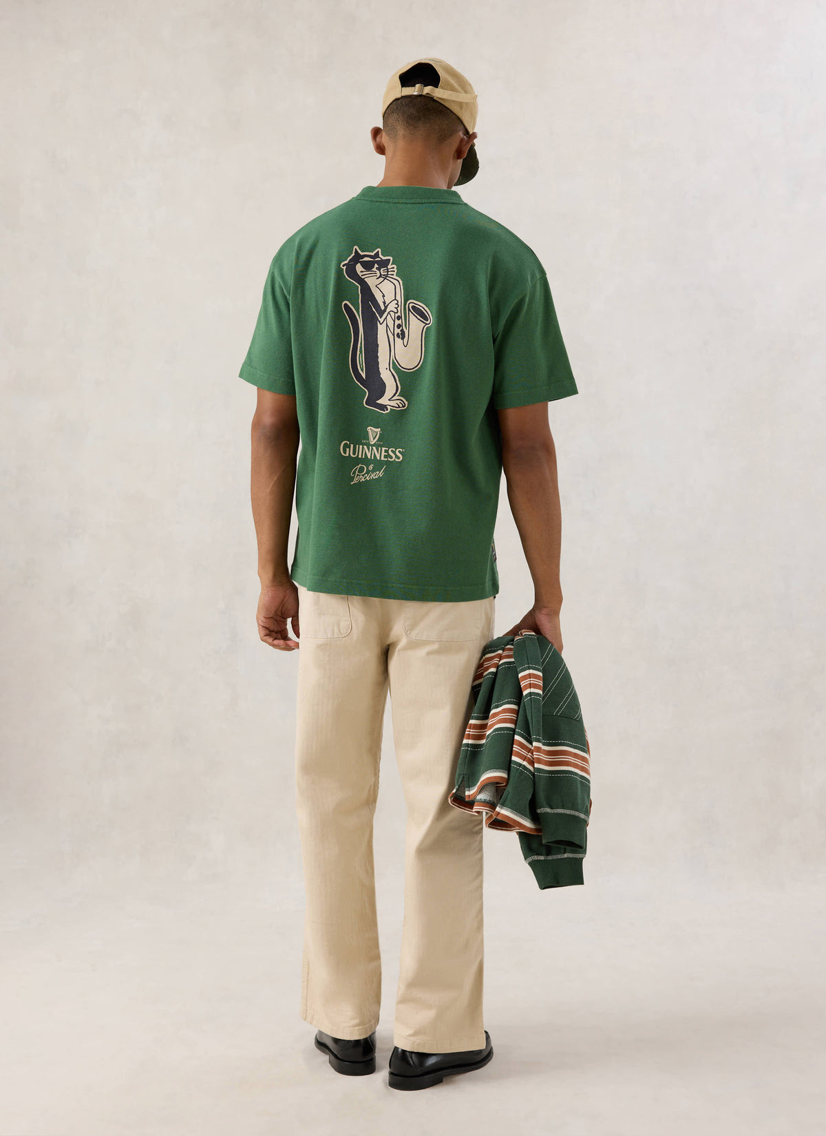 Rear view of a model wearing the forest green Guinness x Percival oversized T-shirt with the saxophonist cat back graphic.