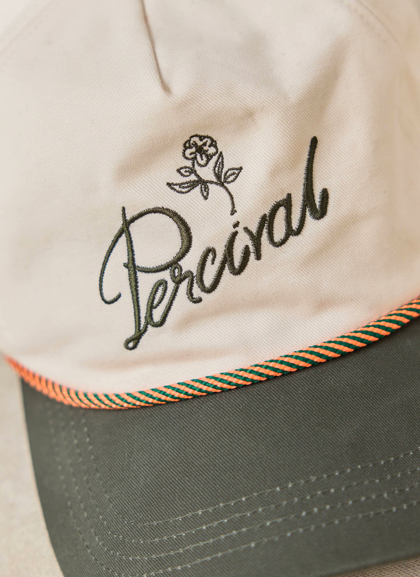 The cream Percival Spencer Trucker Cap in brushed cotton, with green script embroidery and a pop of colour rope detailing.