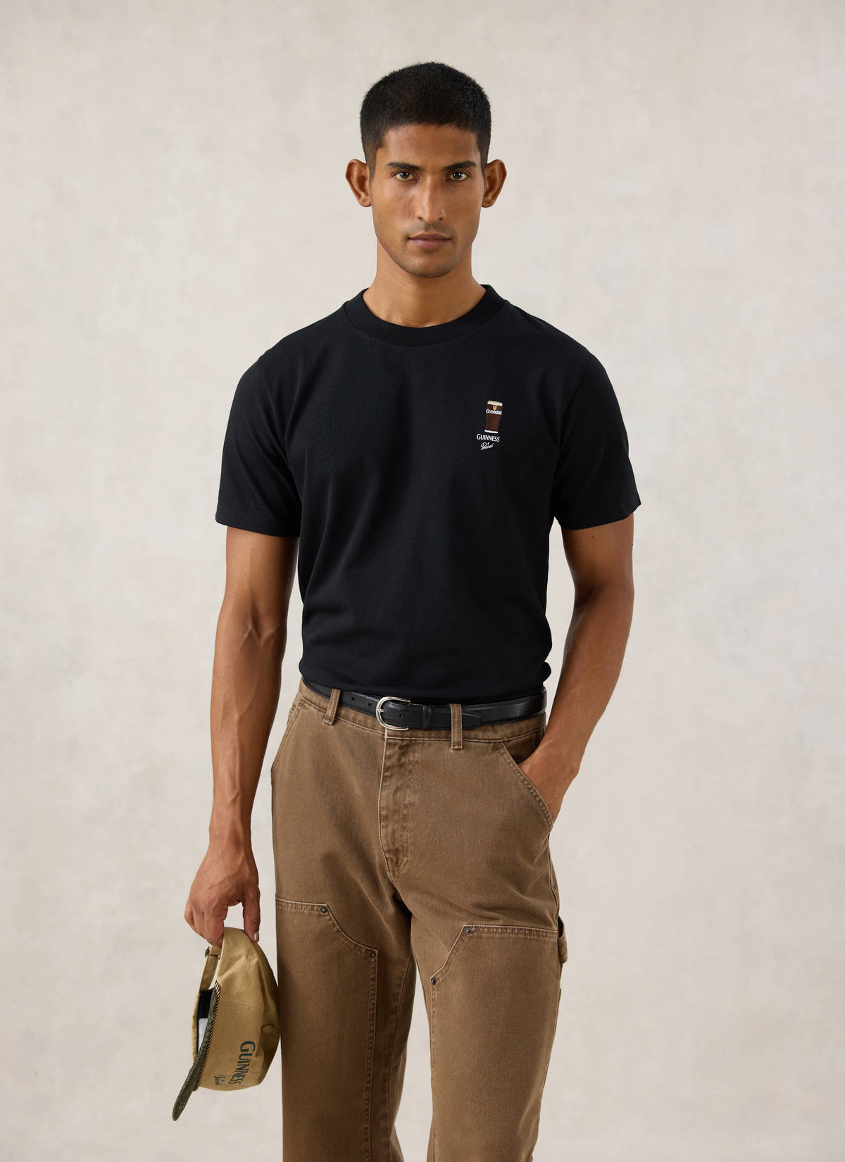 Model wearing the black Guinness x Percival Stout T-Shirt with embroidery, paired with brown trousers.