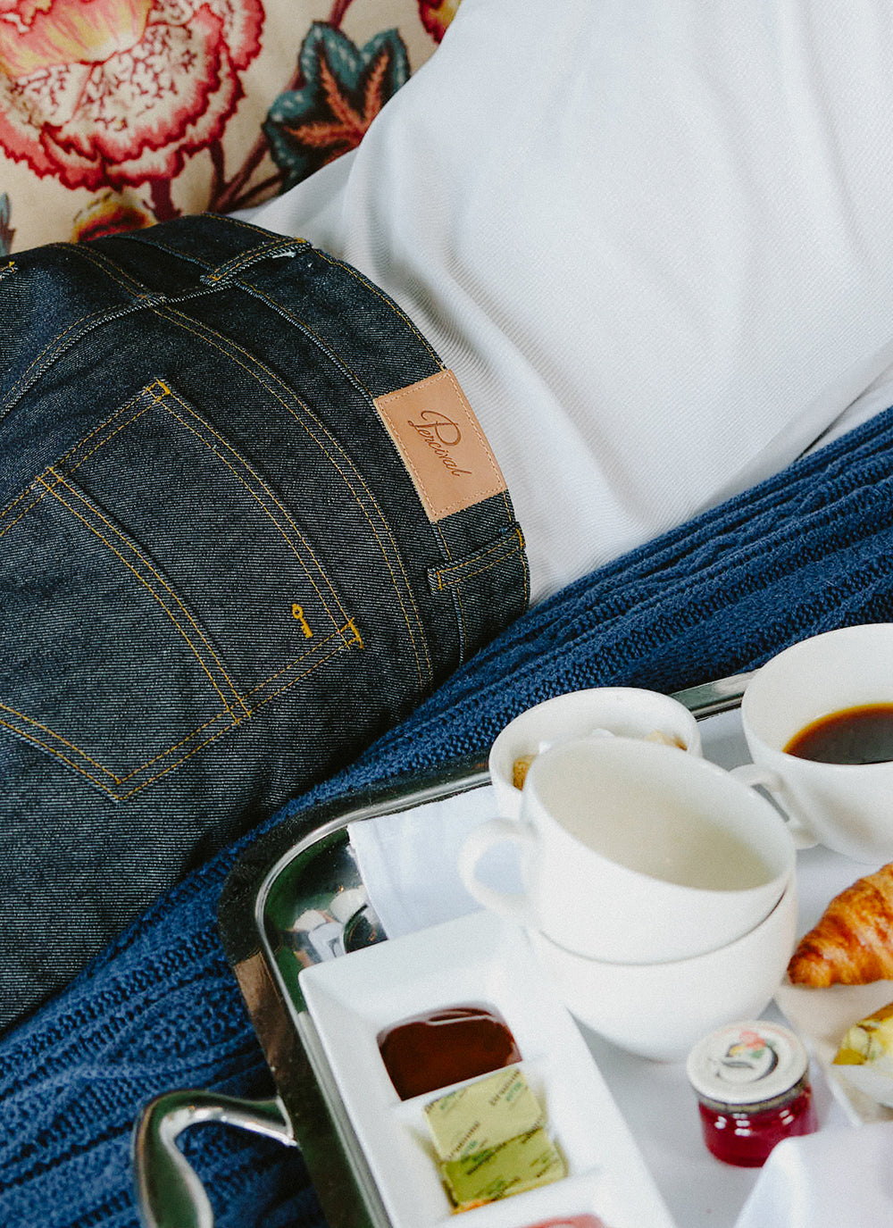 Percival straight leg heritage denim jeans in raw indigo with amber stitching and a leather patch by a breakfast tray.
