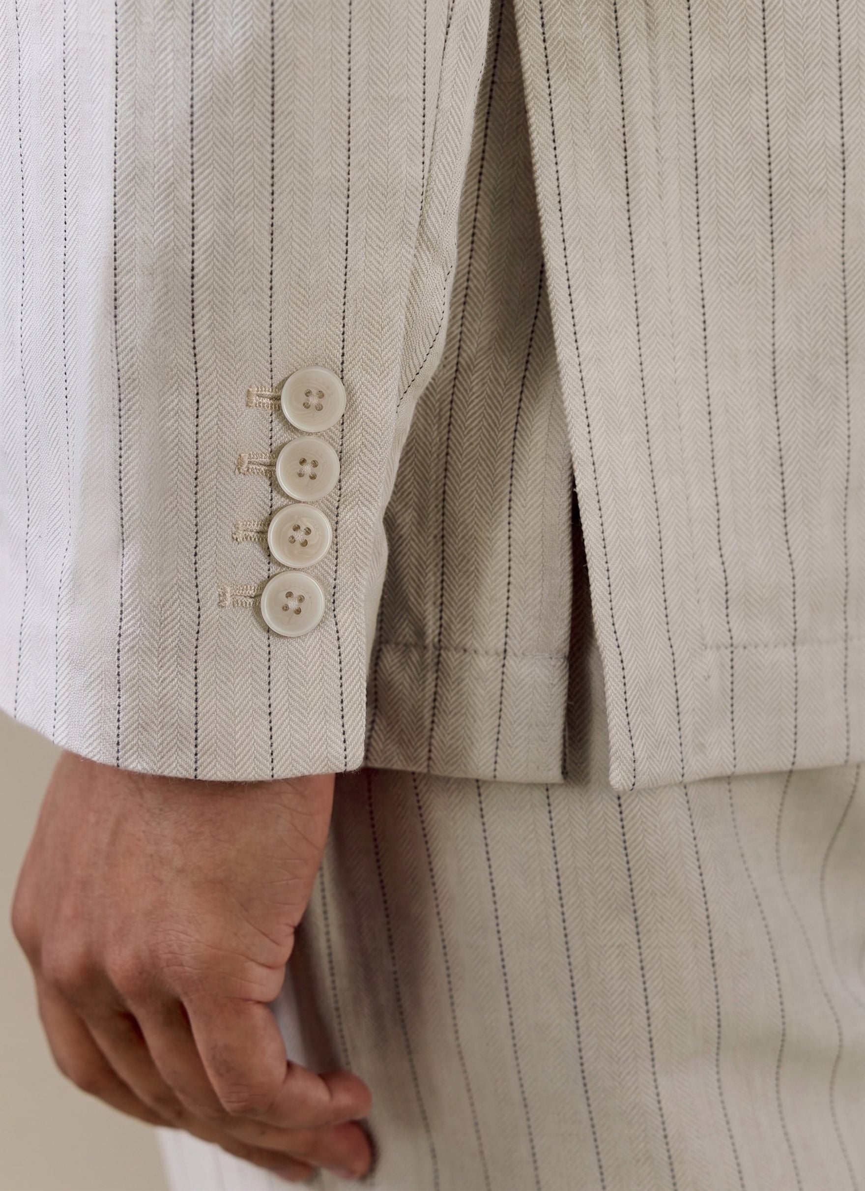 A close-up of the cuff buttons and herringbone texture on the cream striped Percival linen blend tailored blazer.