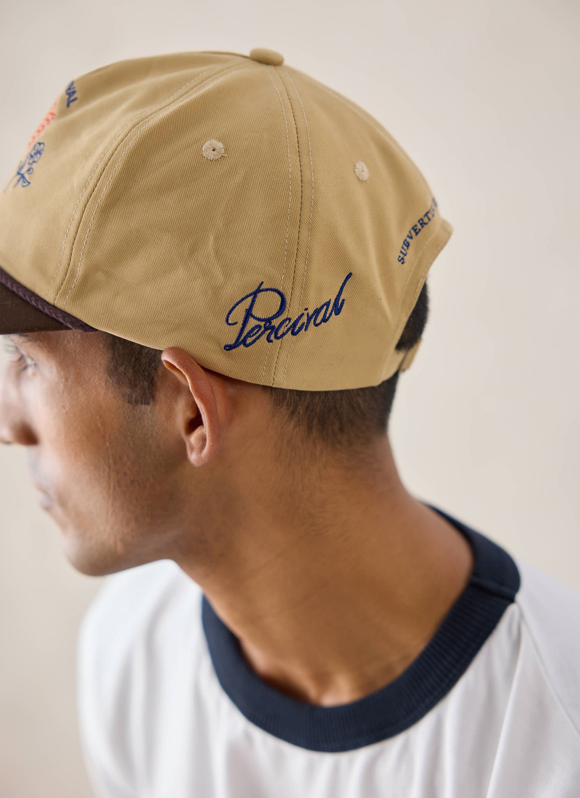 A close-up of a model wearing the tan Tucker Soft Trucker Cap from Percival, highlighting the side embroidery.