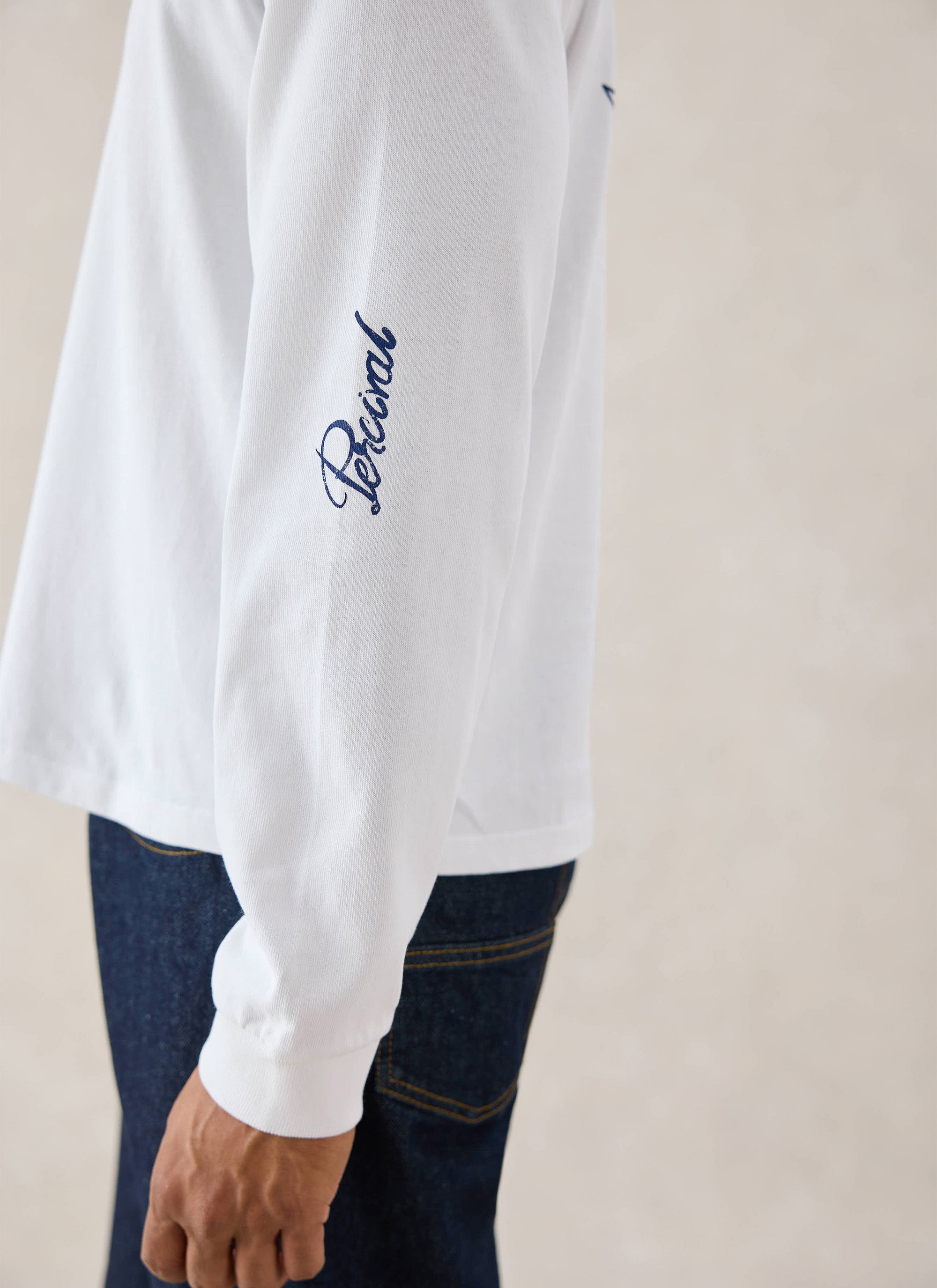 Close-up of a model wearing the white Percival Tucker long sleeve T-shirt, showing the sleeve script embroidery detail.