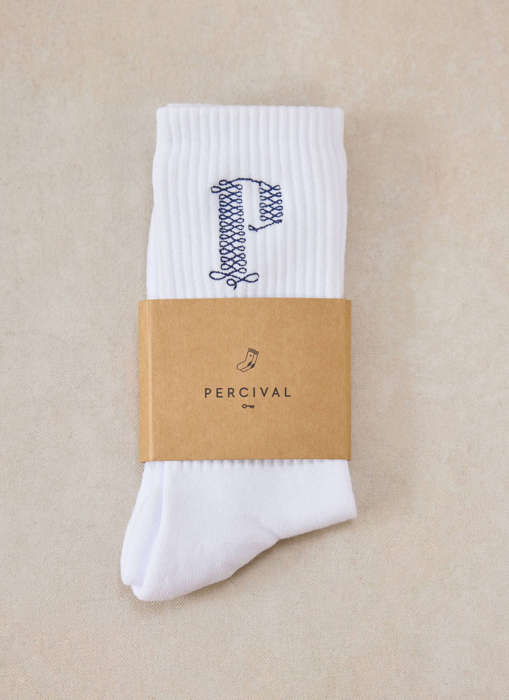 A pair of white Percival Tucker embroidered socks with a branded kraft paper band.
