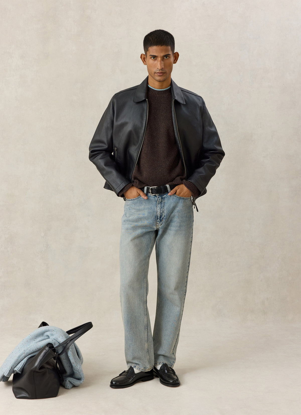 A model wears the Percival black Turner leather zip jacket over a dark knit jumper and light jeans against a studio backdrop.